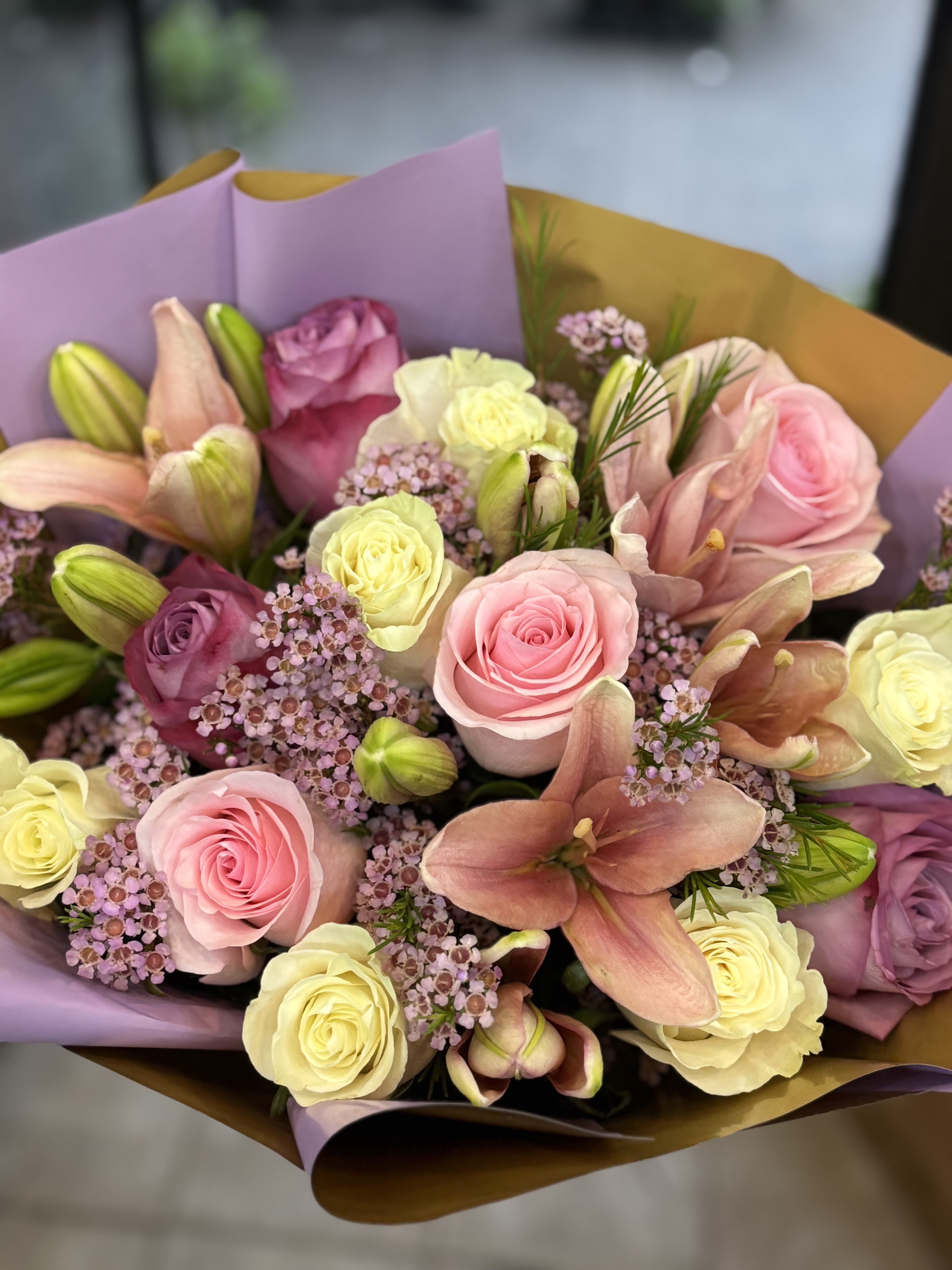 The Princess - Delicate and graceful, this romantic arrangement features soft pink, lavender, and white roses paired with fragrant pink lilies and accented by dainty clusters of wax flower. A perfect blend of charm and sophistication, it's ideal for expressing love, gratitude, or simply brightening someone's day with timeless beauty. Please note: Vase not included. 