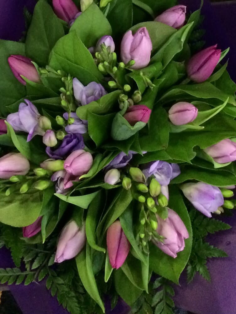 Dutch Impressionist - Array of dutch tulips accented with freesia all nested in a clear cylinder vase wrapped with an aspidistra leaf