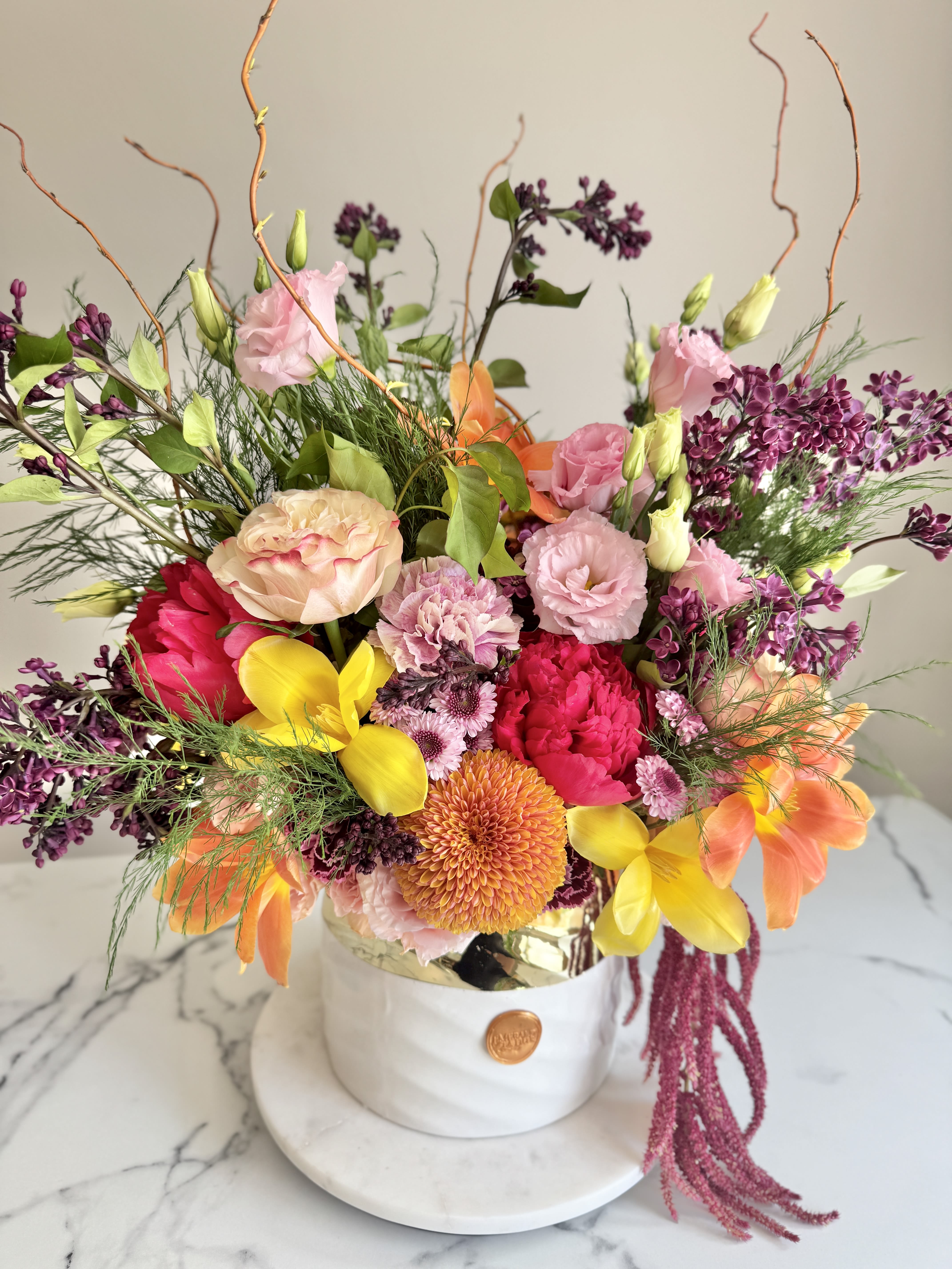 Flora Luxe - A radiant burst of color and texture, Flora Luxe is a lush celebration of spring’s most captivating blooms. Featuring a vibrant mix of roses and a medley of colorful flowers, this garden-style arrangement overflows with elegance and personality. Nestled in a white ceramic vessel, this large floral piece is perfect for birthdays, celebrations, or simply bringing abundance of joy to any space.