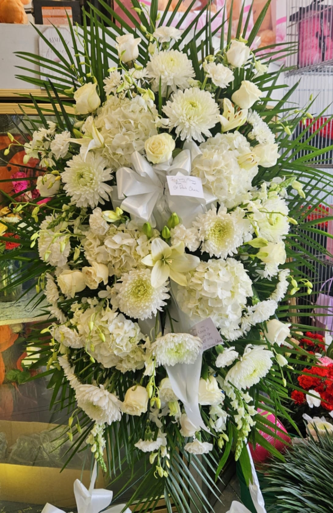 Big All White Funeral Spray Big All White Funeral Spray - This is an all white funeral spray with white orchids, white roses, white chrysanthemums, white hydrangeas, white snapdragons, white lilies, lots of white flowers and babys breath with lots of greenery on a large stand with a big white bow. A very beautiful and full funeral spray to cherish and remember a loved one going to Heaven. A very beautiful and full floral spray.