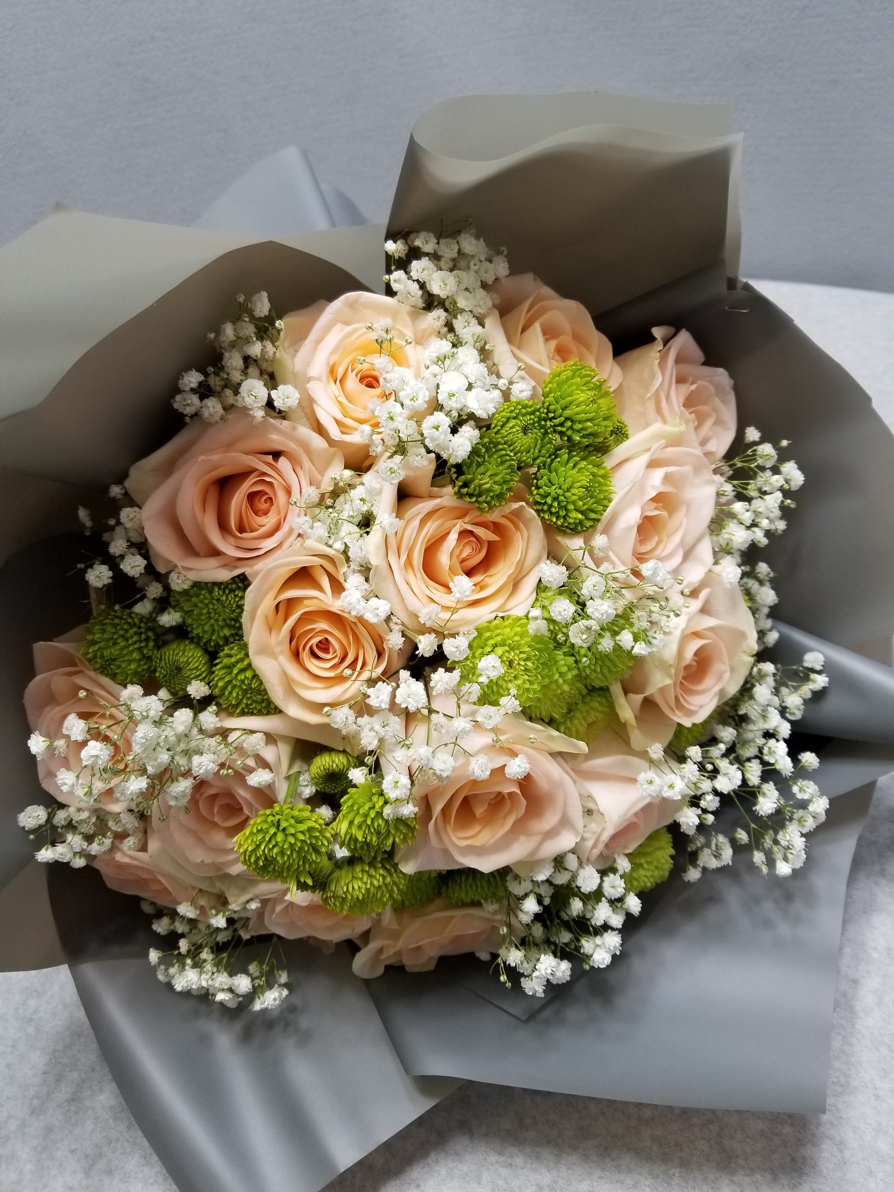 Phoenix Cushions - Phoenix Cushions is a wrapped bouquet designed of peach roses, green chrysanthemum cushions, and baby's breath.
