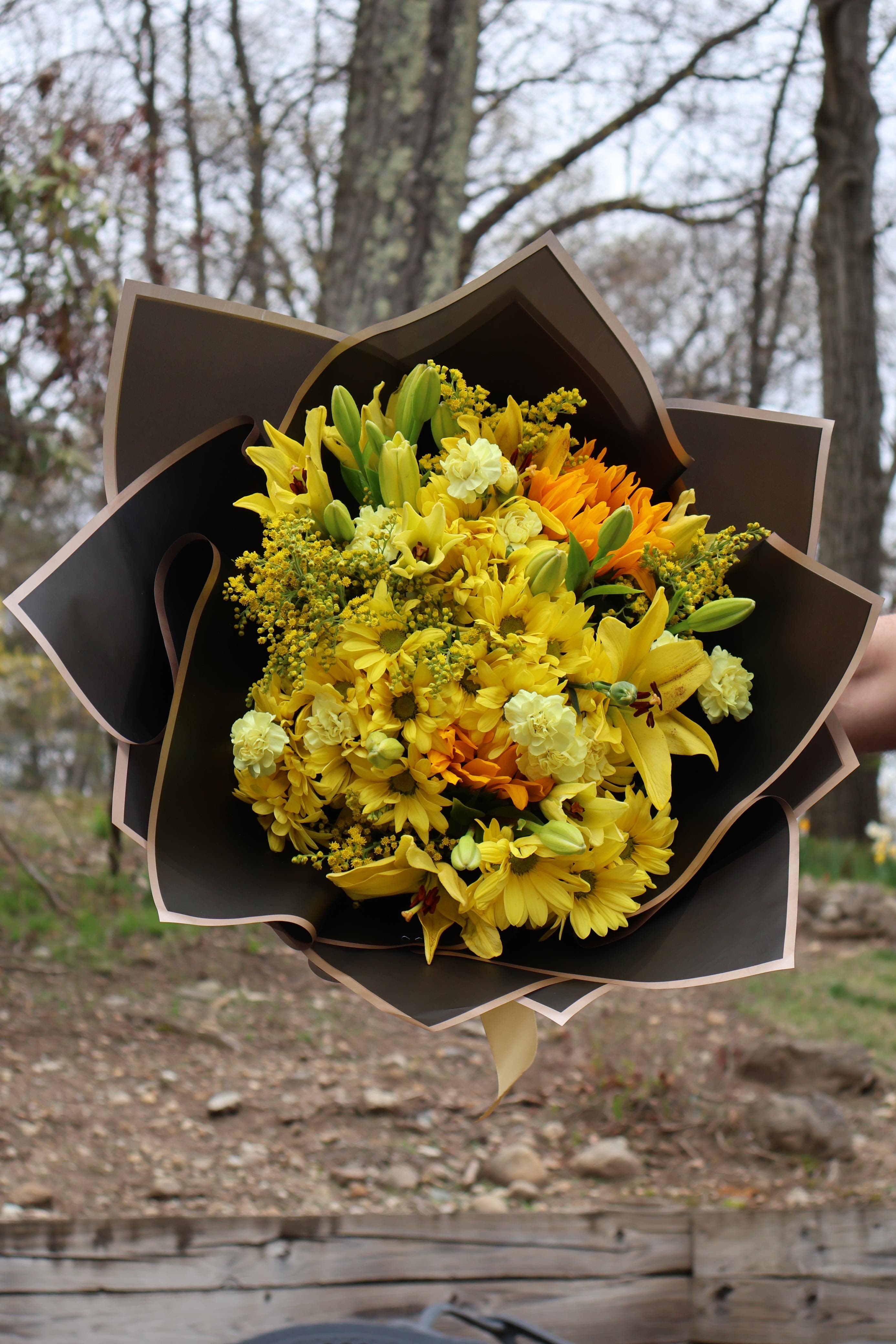 Sun kissed  - A cheerful burst of sunshine, this bouquet features yellow lilies, golden daisies, and soft carnations—wrapped in sleek paper for a bright, joyful presentation.