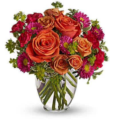 A Warm Welcome - Warm orange roses, hot pink matsumoto asters and hot pink carnations are accented with bright greenery in a clear glass vase.