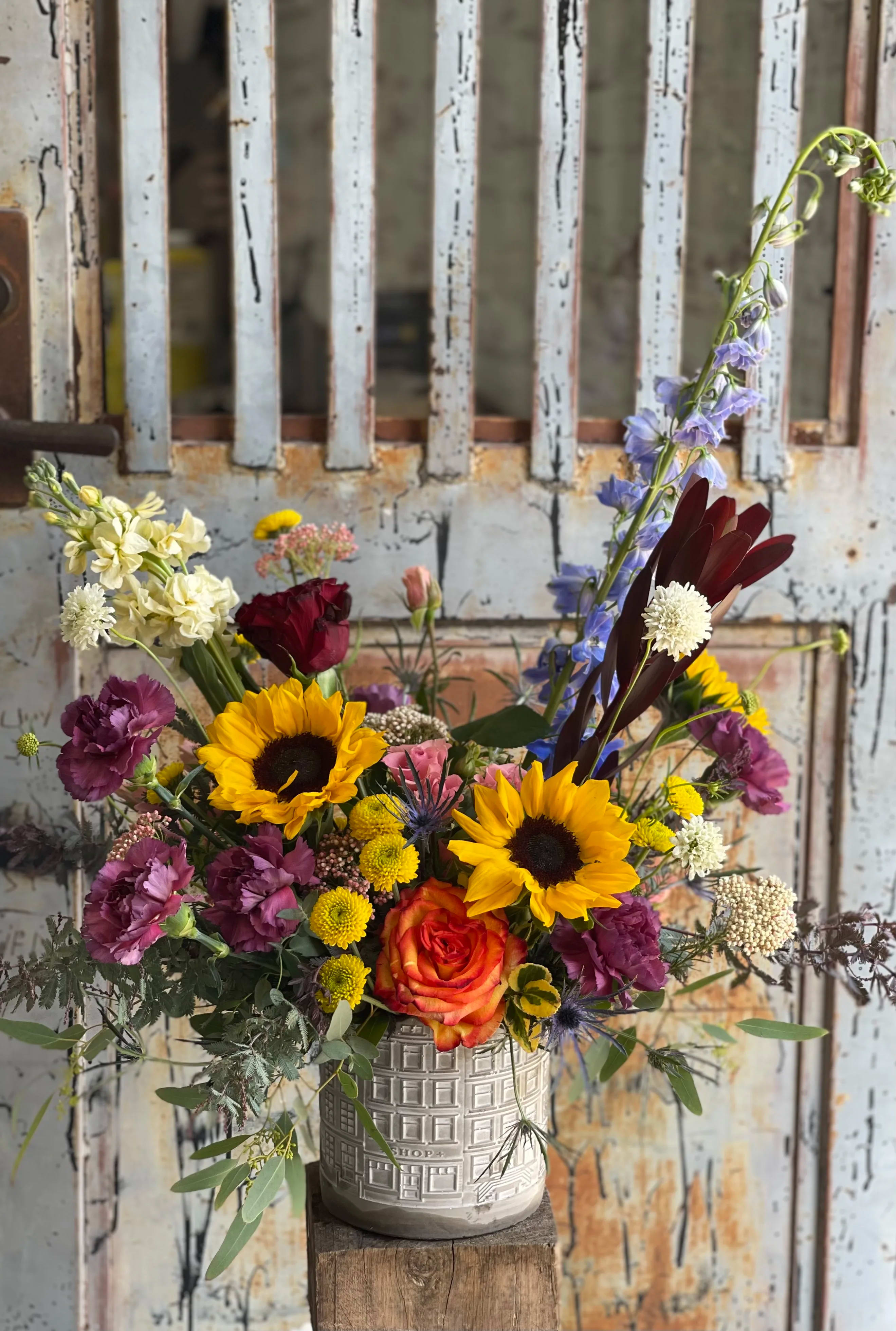 Sunflower Circus  - This arrangement is uniquely crafted with the love of sunflowers and orangey yellow hues with a touch of purple accents to give a lovely contrast. Arrangement and vase may vary depending on product availability.