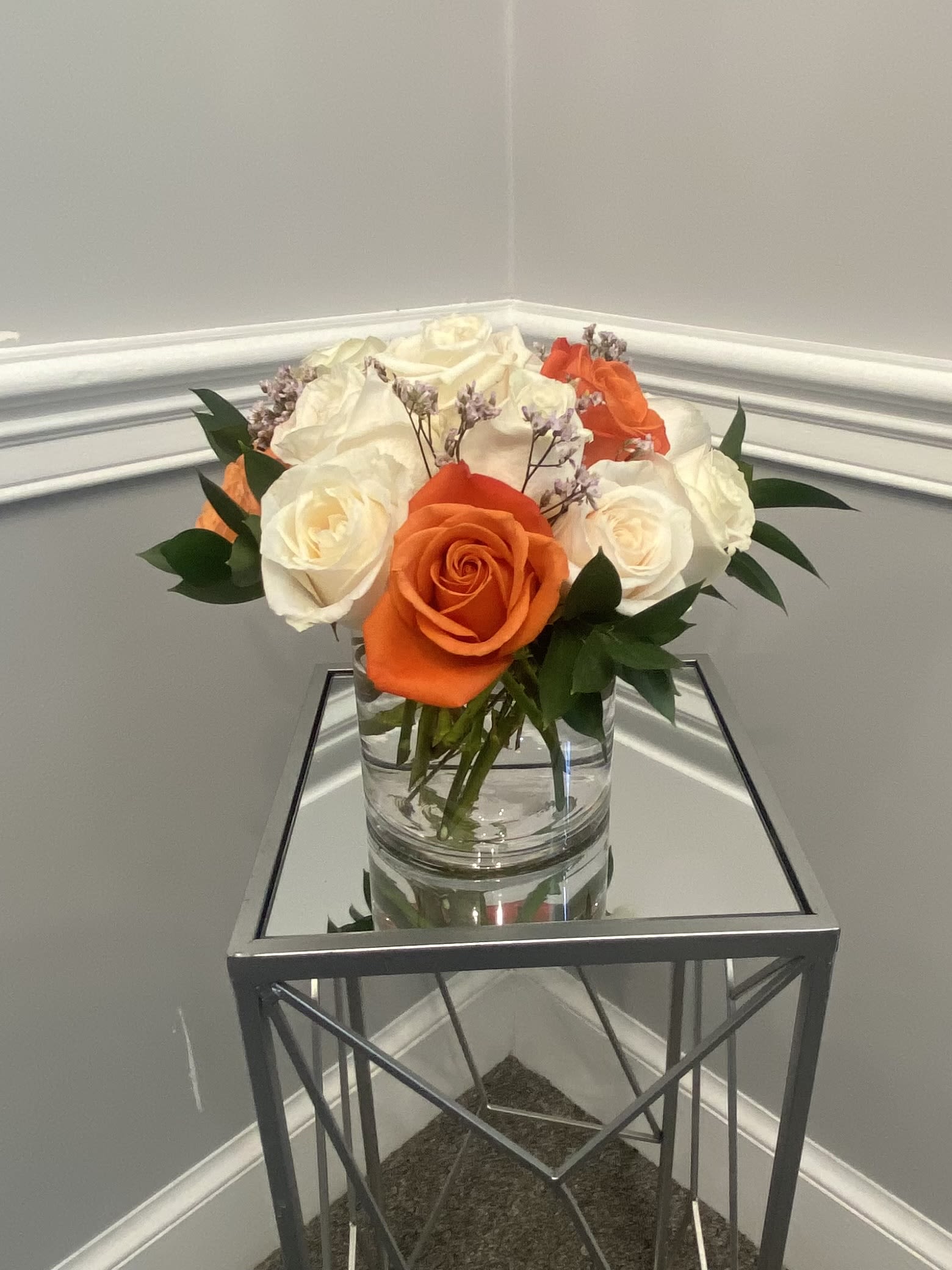 Blushing Peach Melody - This flower arrangement captures the soft, warm glow of dawn. Light orange and cream roses are artfully arranged with lush greenery and delicate filler flowers within a sleek glass cylinder vase, creating a look that's both modern and effortlessly elegant. It's the perfect floral arrangement for home décor, a thoughtful gift for her, or a stunning centerpiece for any special occasion.