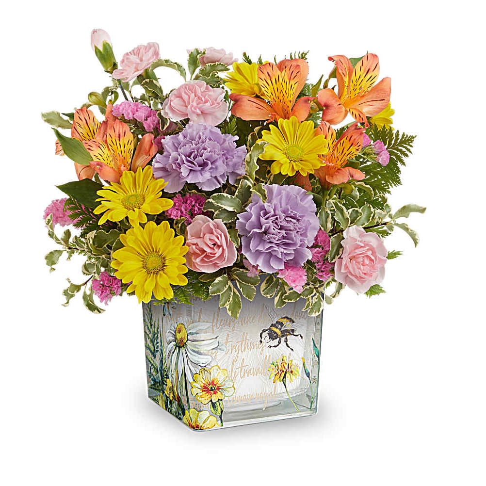 Floral Buzz Bouquet - Like a bee dancing through a hidden garden, this enchanting bouquet of orange, lavender, and yellow blooms in a vintage-inspired glass cube makes for a truly magical gift. This delightful arrangement features vibrant orange alstroemeria, lavender carnations, miniature pink carnations, yellow daisy spray chrysanthemums, and pink sinuata statice, all beautifully accented with leatherleaf fern and pitta negra. It is presented in The Floral Buzz Cube, making it a charming addition to any tablescape.