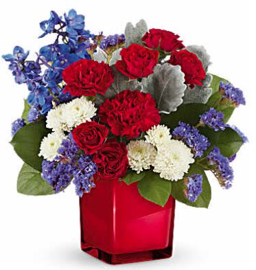 Radiant Colors - Embrace a timeless color palette of radiant red, white, and blue blooms, elegantly presented in a striking scarlet color splash cube.  Discover a masterpiece featuring vibrant red spray roses, classic red carnations, elegant blue delphinium, white button spray chrysanthemums, blue sinuata statice, and accented with lush dusty miller and salal. Delivered in Teleflora's Scarlet Color Splash Cube, it's a testament to refined beauty and contemporary style.