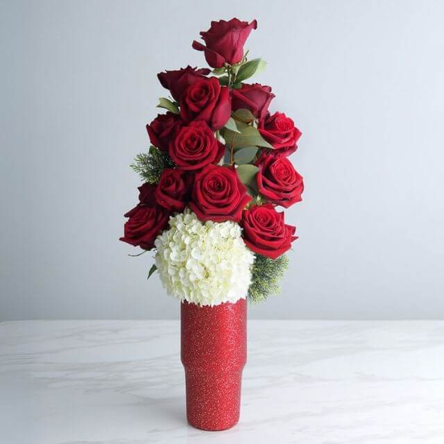 Sparkle Sparkle - A striking vertical arrangement with flowers such as rich red roses, soft hydrangea, and textured greens.