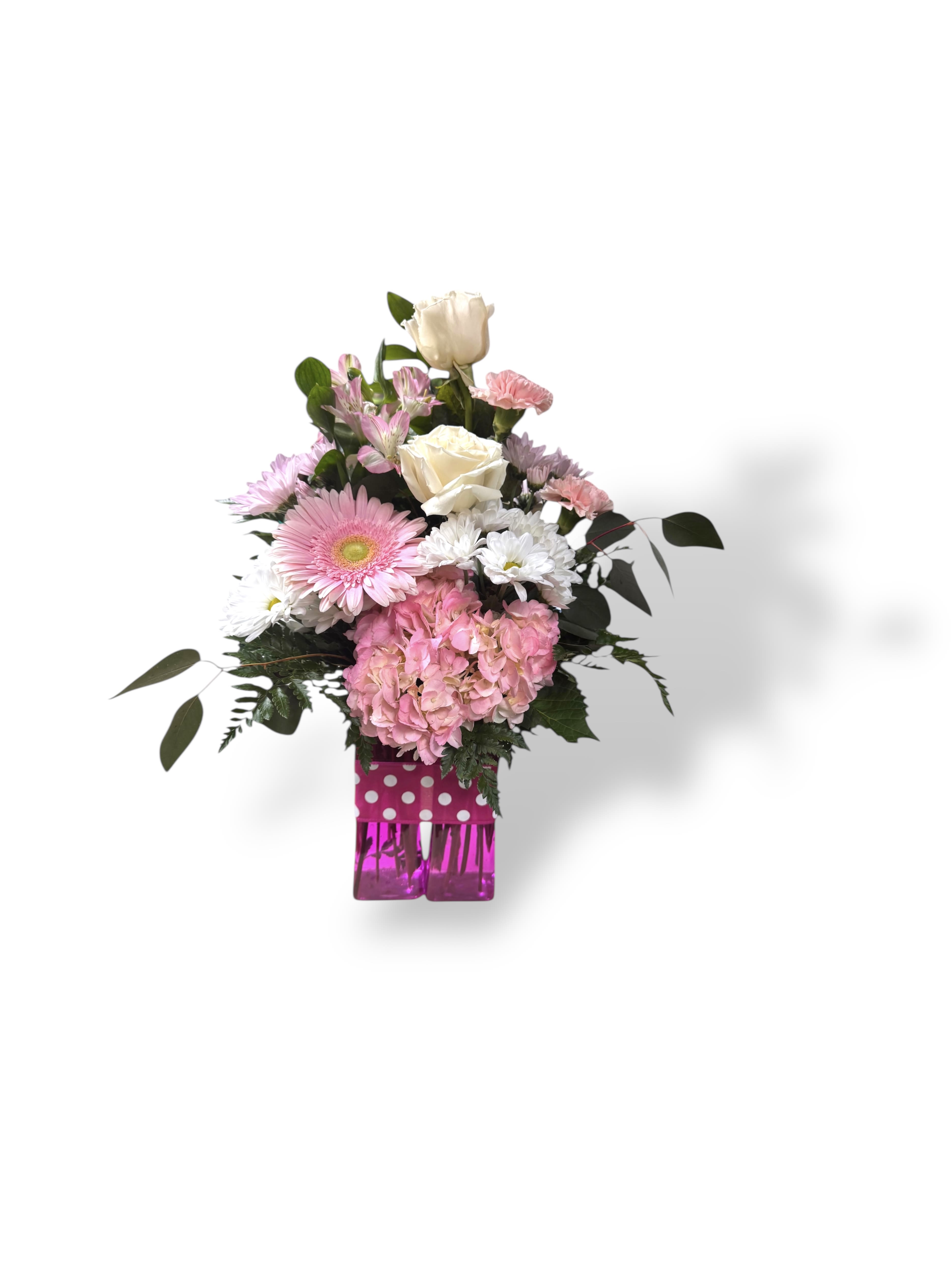 Pink Parade -  Bursting with charm and unapologetic cheer, Pink Parade is a joyful celebration in bloom. A lush pink hydrangea anchors the composition, joined by a playful pink daisy and a swirl of daisy pom-poms in pink and soft lavender. Two elegant white roses add a hint of classic beauty, Tied with a polka-dotted ribbon and standing proudly in a hot pink vase, this design is a bubbly, whimsical statement perfect for anyone who loves life in full color.