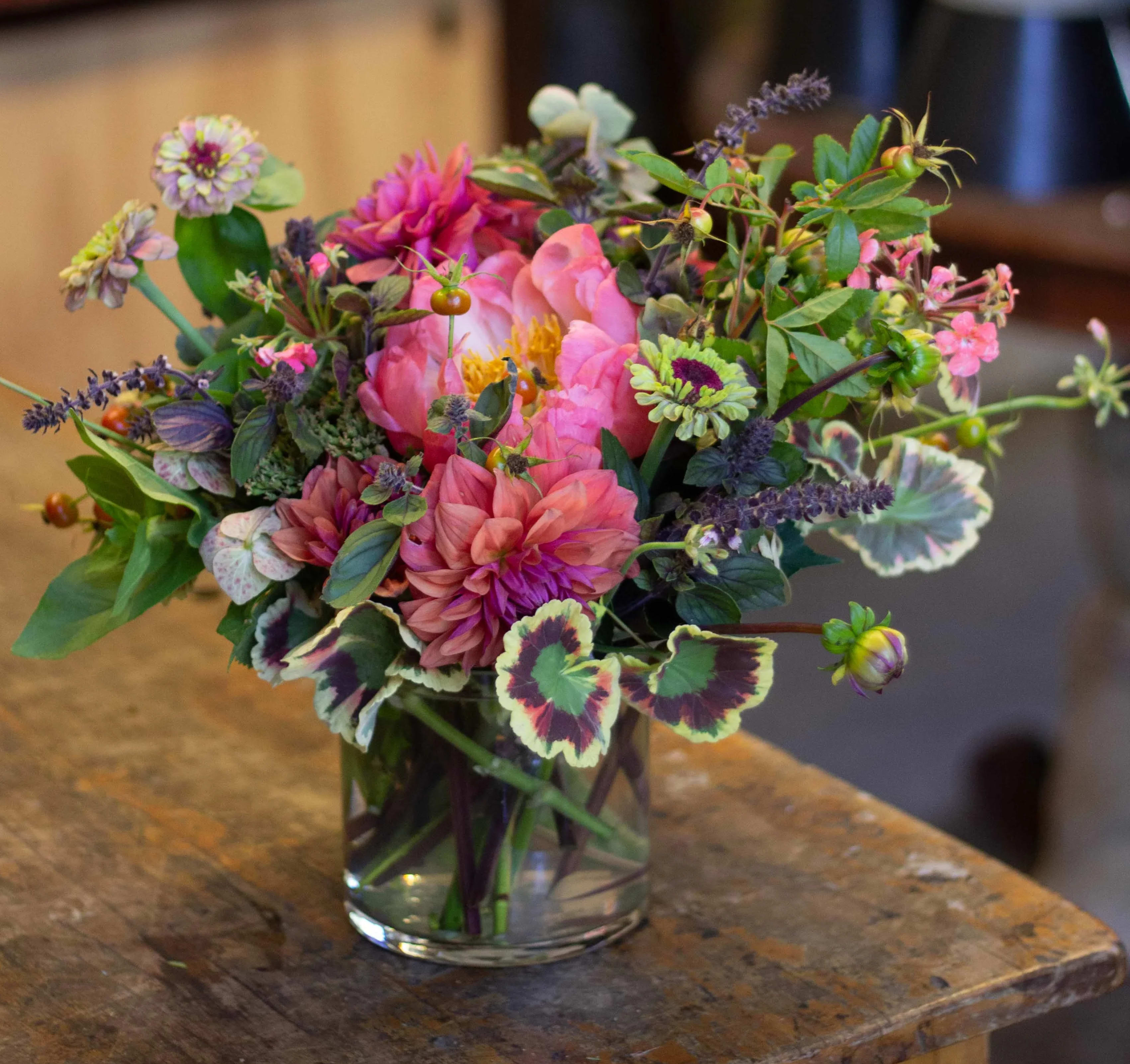 Sana - A lush arrangement of brightly colored seasonal flowers, geranium and berries. 