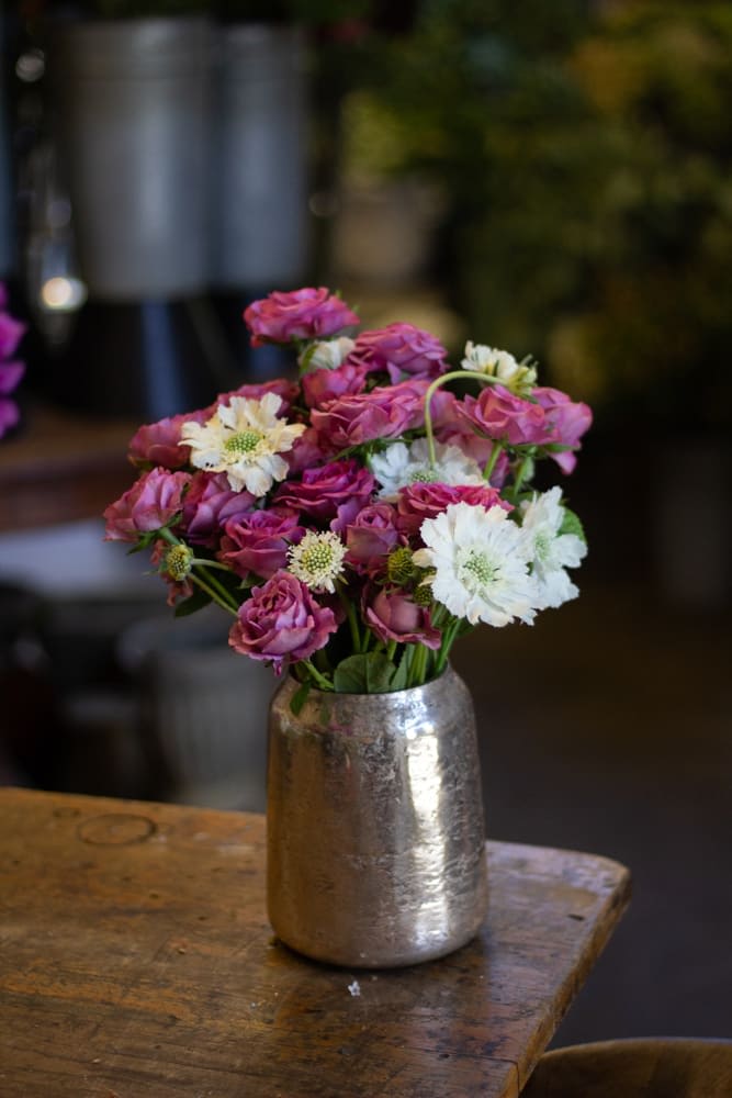 You're cute - An assortment of spray garden roses with another neutral colored flower in a tall cylindrical mercury vase. 