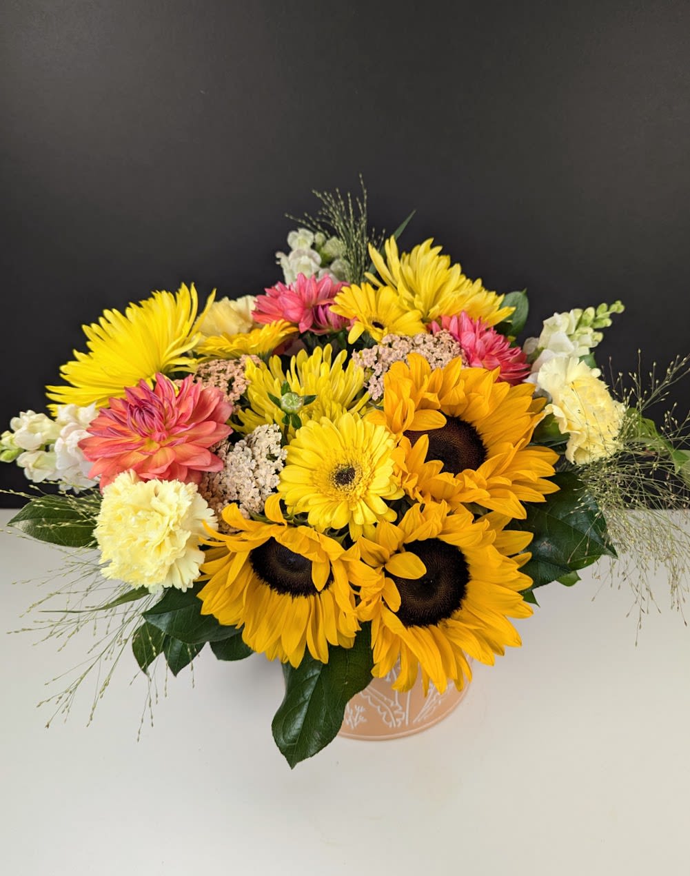 Summer’s Watering Can - Summer’s Watering Can A cheerful burst of golden light, Summer’s Watering Can captures the easy joy of a sun-drenched garden. Arranged in a charming metal watering can, this design brings a warm and whimsical touch to any space, Featuring:  -Sunflowers -Yellow gerbera daisies -Yellow carnations -White snapdragons -Peachy dahlias -Yellow mums  Perfect for celebrating the heart of summer or brightening someone’s day with garden-inspired charm.  