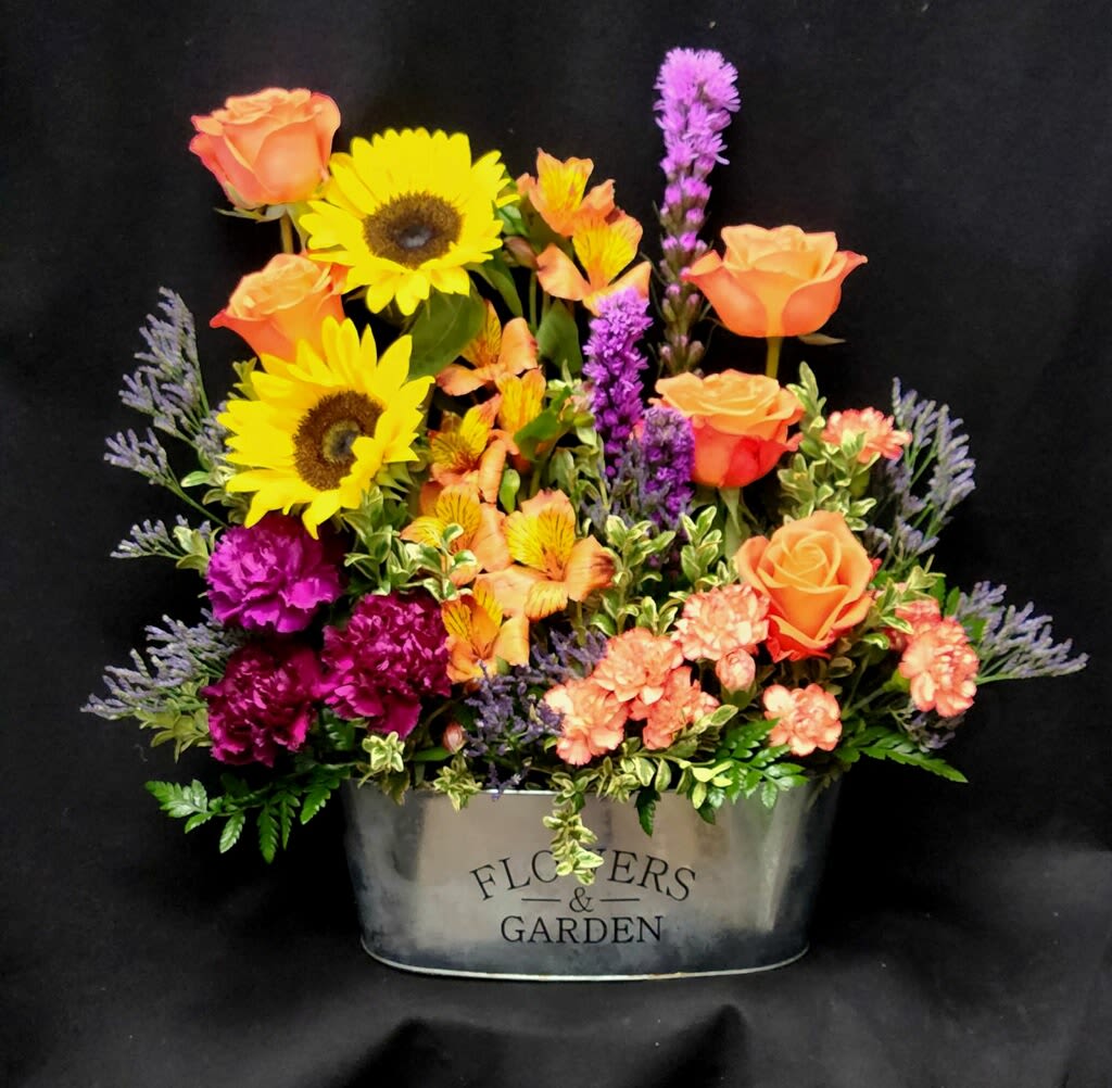 Summer fun! - Beautiful tin vese filled with vibrant colors, including: orange roses, sunflowers, bourgandy carnations, orange alstromeria, liatris, purple misty as a filler, orange mini carnations and mixed lush greens.