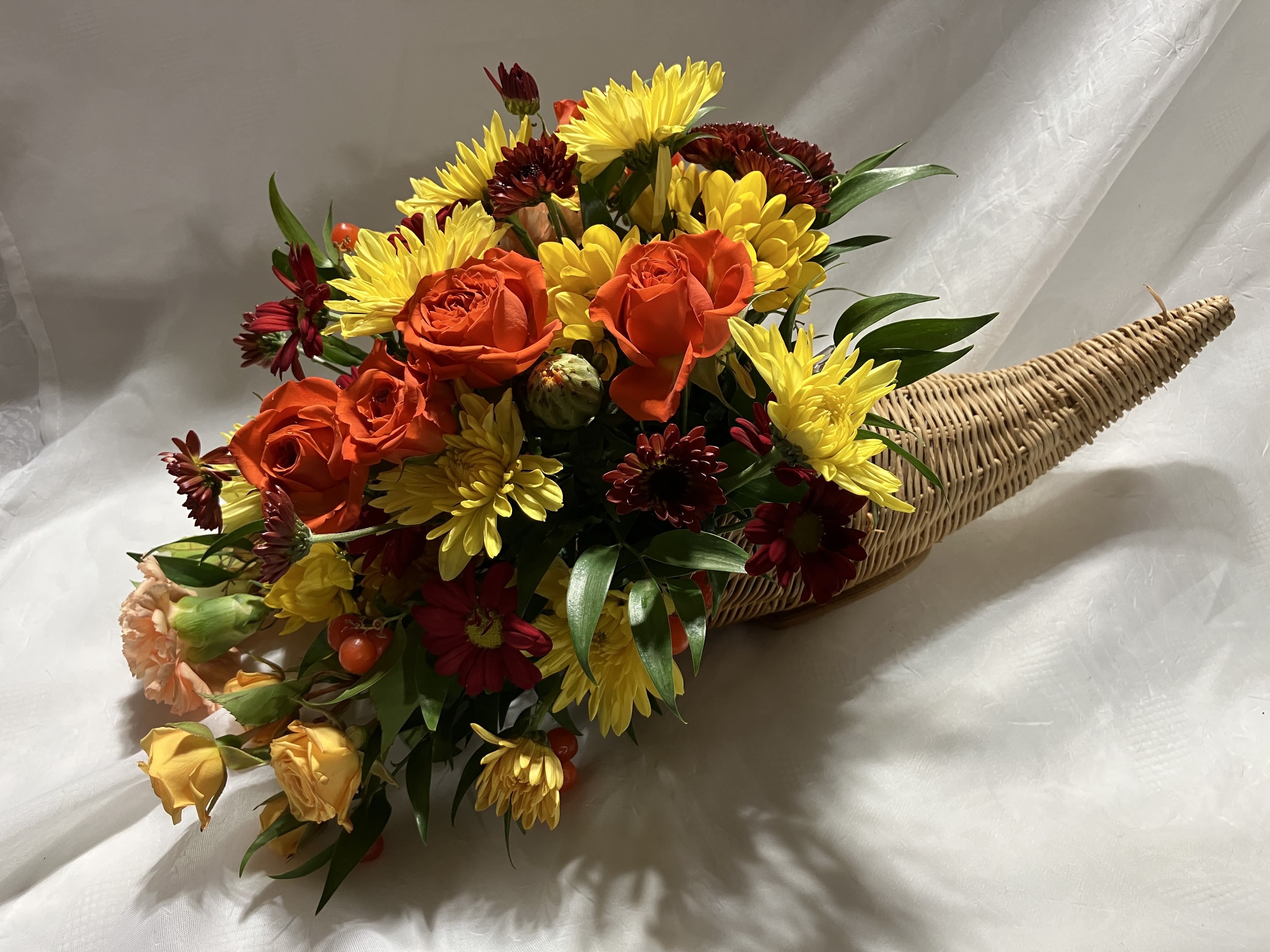 Cornucopia centerpiece - Cornucopias are synonynous with Thanksgiving--the horn of plenty wicker basket.  Celebrate the bounty of the season with this centerpiece of spray roses, carnations, mums and others, as available.    
