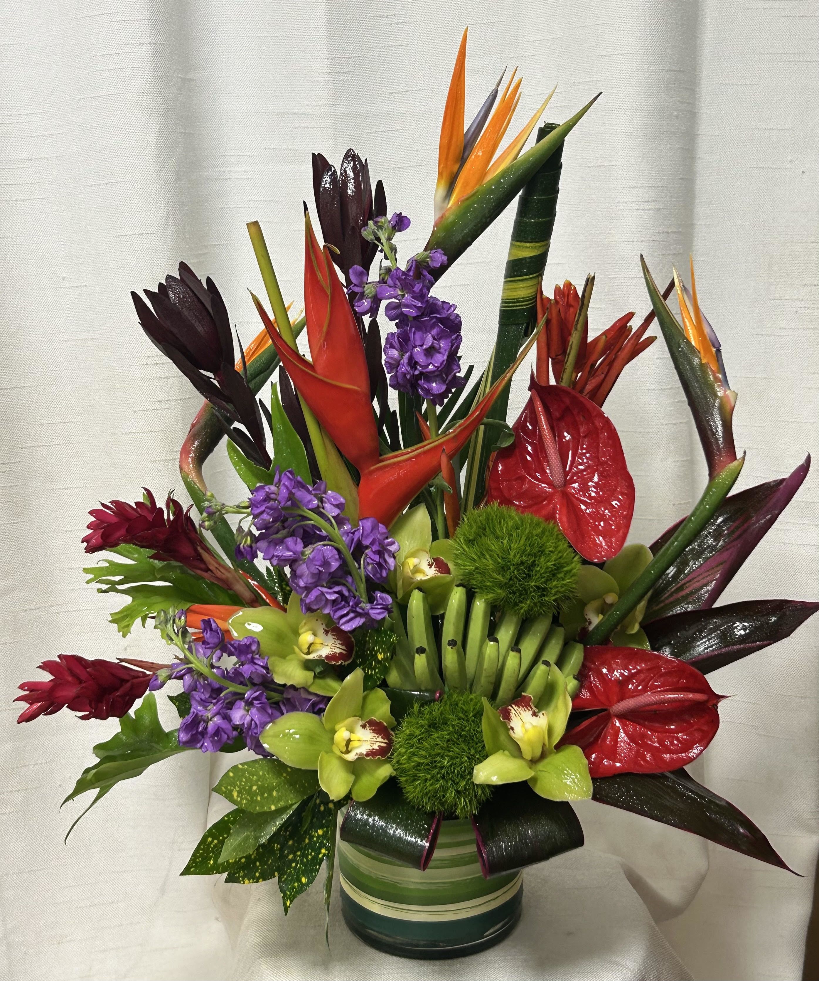 Hawaiian luau  - Experience the vibrant beauty of the tropics with our Hawaiian Luau tropical flower arrangement. This stunning ensemble features a captivating combination of exotic flowers, including anthurium, birds of paradise, and cymbidium orchids, all elegantly arranged with lush tropical greens.  