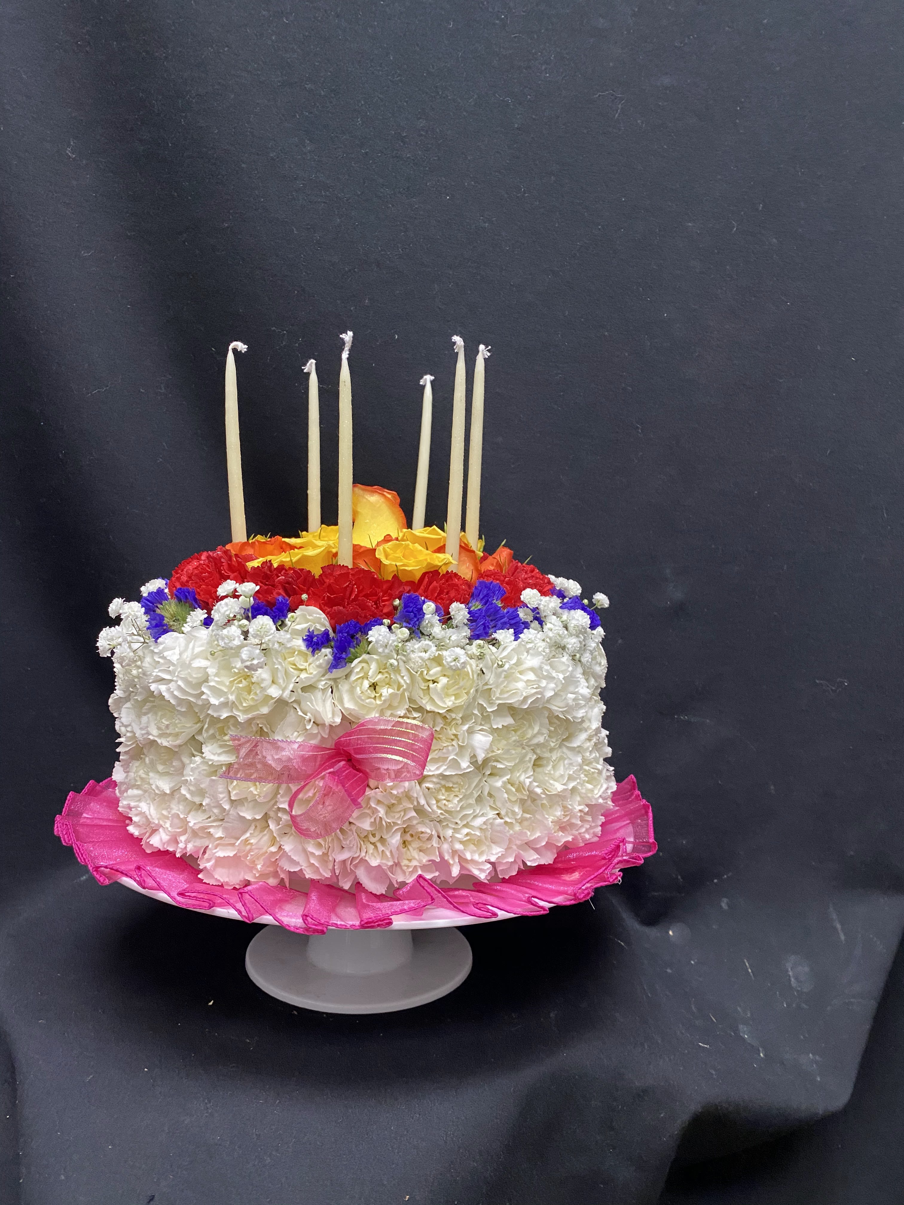 Celebrating with you - Cake on a pedestal white mini carnations, red mini carnations, purple statice, orange spray roses, 1 yellow rose, baby's breath with hot pink ribbon and bows