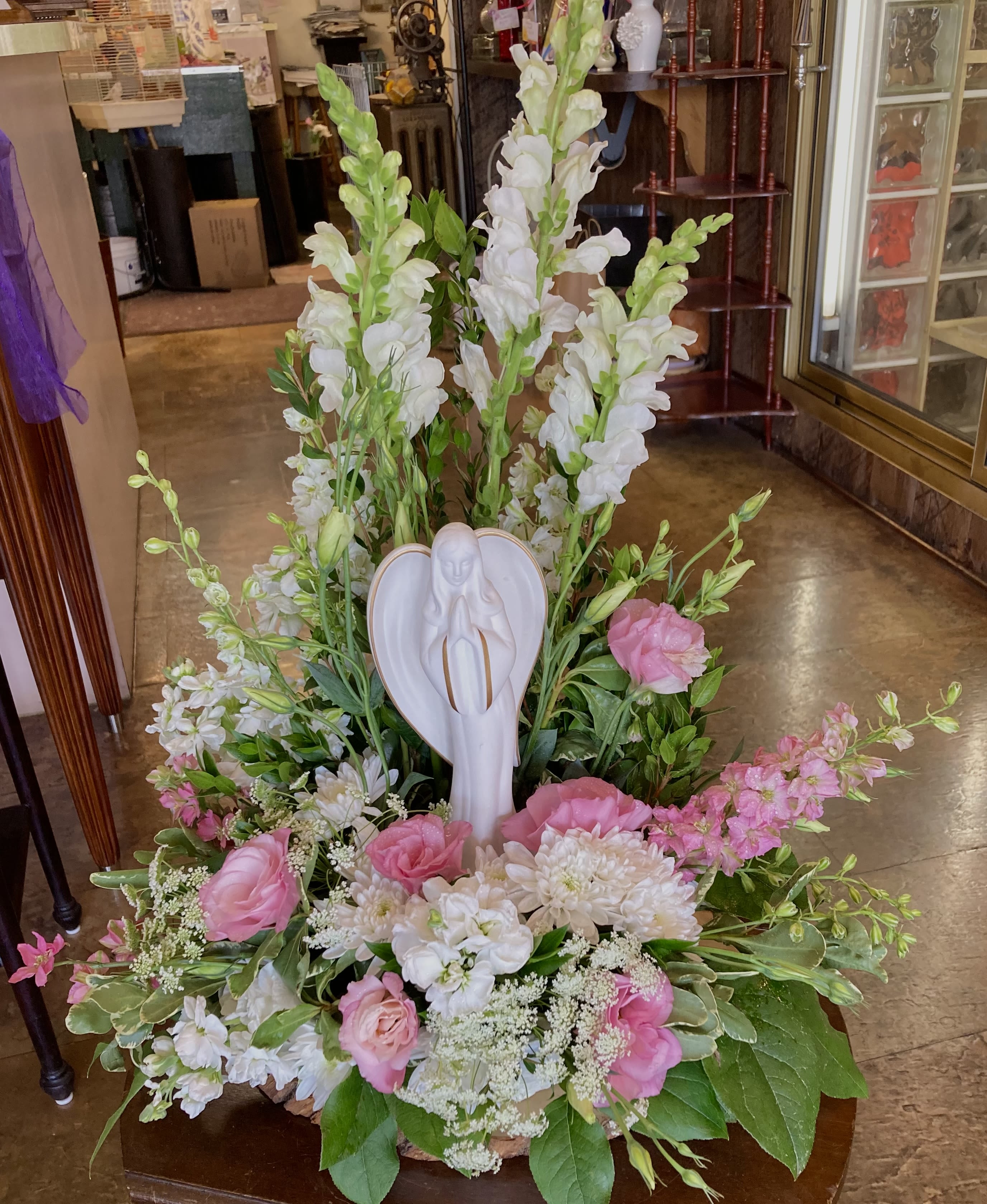 Poised Angel Poised Angel - Soft shades of pink and white blooms surround this poised angel. A timeless expression of love, comfort, and peace- perfect for memorials, sympathy gestures, or spiritual occasions. This arrangement features snapdragons, larkspur, lisianthus, queen anne's lace, stock, and nice greenery, creating a serene, fresh picked feeling.