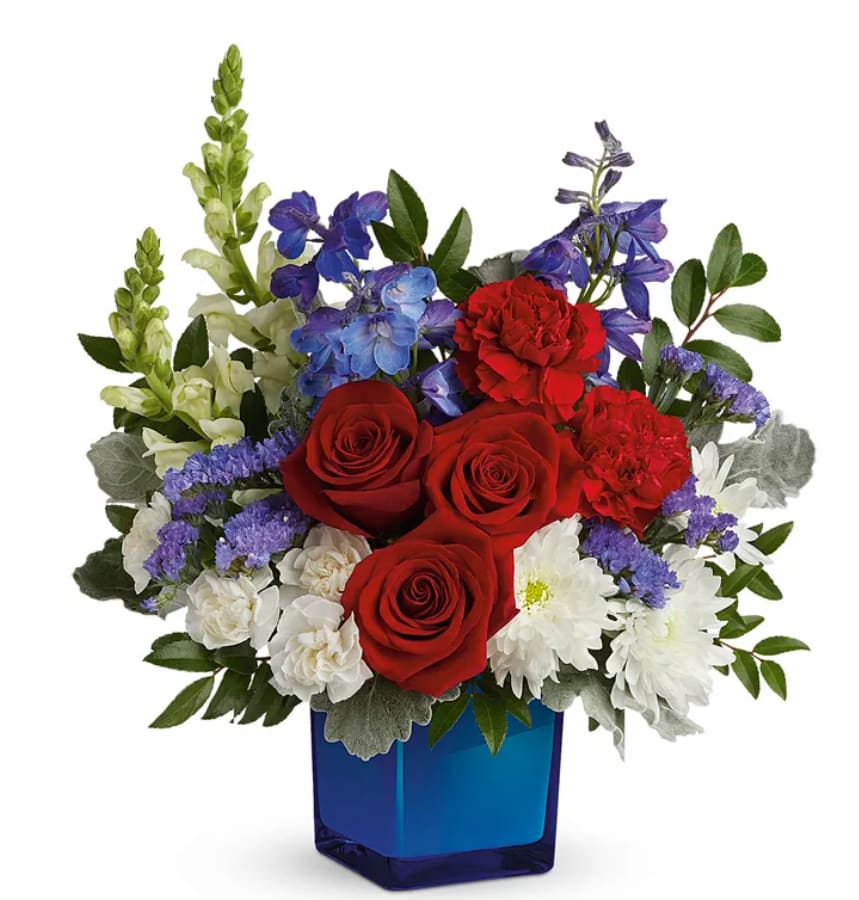 Red, White, and Bloom - These patriotic and beautiful colors of red roses, red carnations, white miniature carnations, blue delphinium, white snapdragons, white cushion chrysanthemums, and lush floral greenery. Presented in a blue glass cube vase, this arrangement is a perfect gift for Father´s Day, Memorial Day, 4 July.