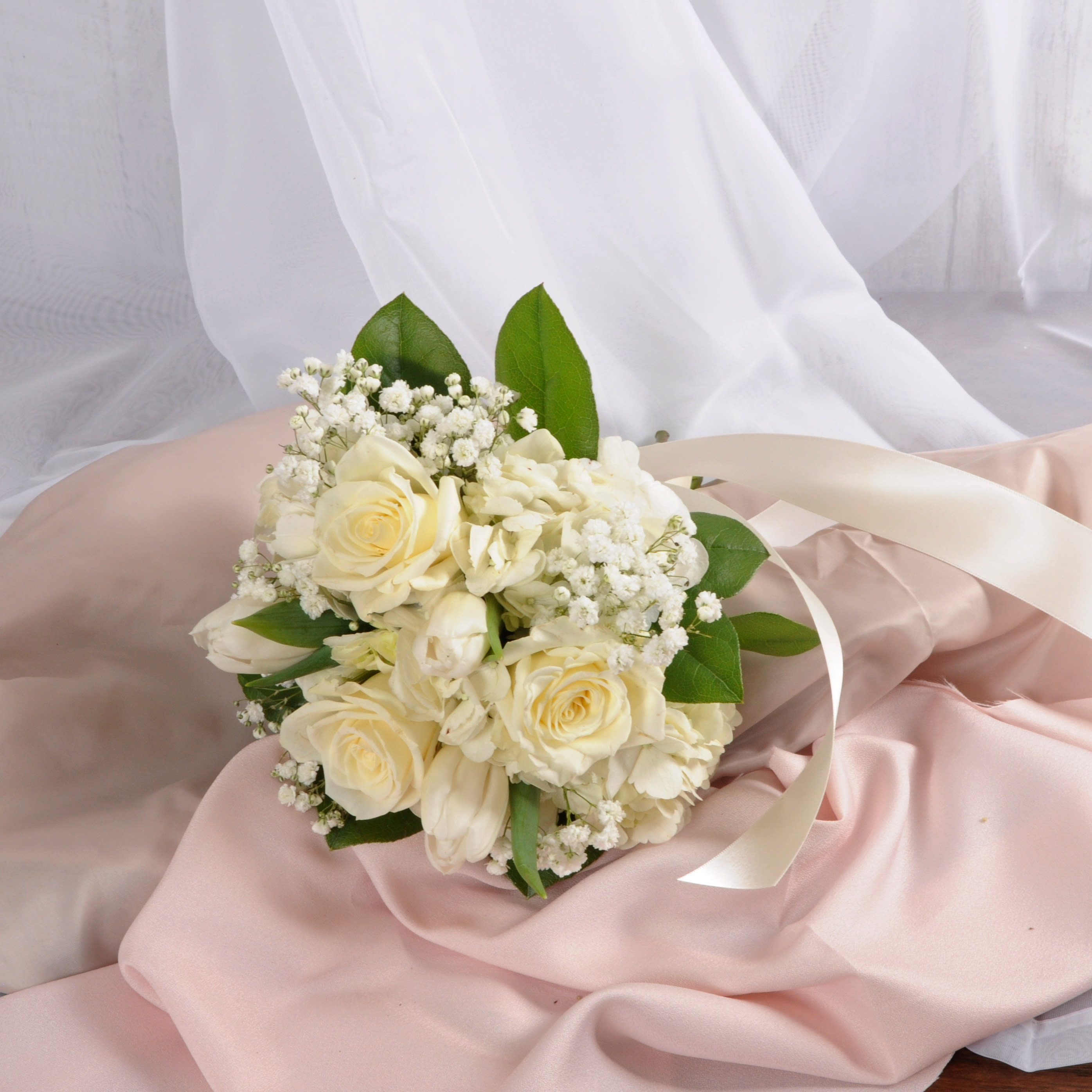 Hand-tied bouquet of ivory roses and white flowers with ribbon on pink fabric