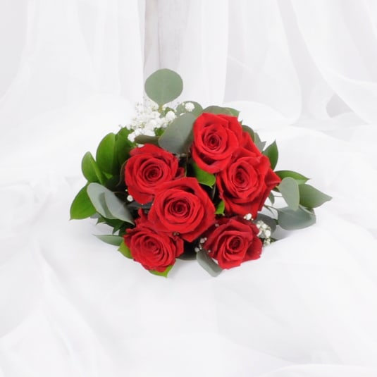 Hand-tied bouquet of red roses with white filler flowers on white fabric