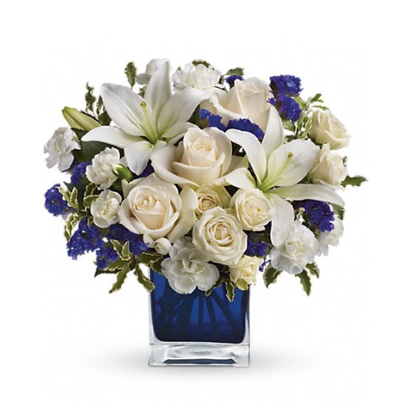 Sapphire Skies Bouquet [TEV25-3A] - Send someone a bit of heaven with this beautiful bouquet. Luxurious crème roses and pure white lilies paint a peaceful picture inside a sapphire blue cube.  Crème roses, white asiatic lilies and white miniature carnations are mixed with bursts of purple statice and green pitta negra. Delivered in a glass Cube.  Approximately 12&quot; W x 11 1/2&quot; H  Orientation: All-Around      As Shown : TEV25-3A