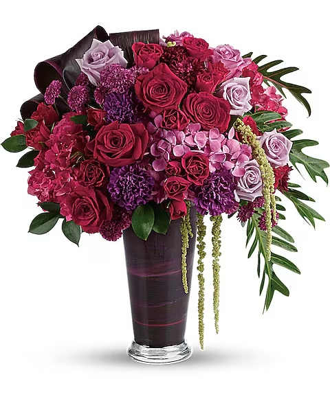 Cascading Elegance Bouquet - A dramatic display in jewel-toned roses and hydrangea in a sophisticated vase, this majestic bouquet will take their breath away.  Dark pink hydrangea, lavender hydrangea, lavender roses, light lavender roses, red roses, red spray roses, purple carnations, purple button spray chrysanthemums, and purple cushion spray chrysanthemums are arranged with hanging green amaranthus, israeli ruscus, xanadu philodendron leaves, and red ti leaves. Delivered in a glass romanesque vase.