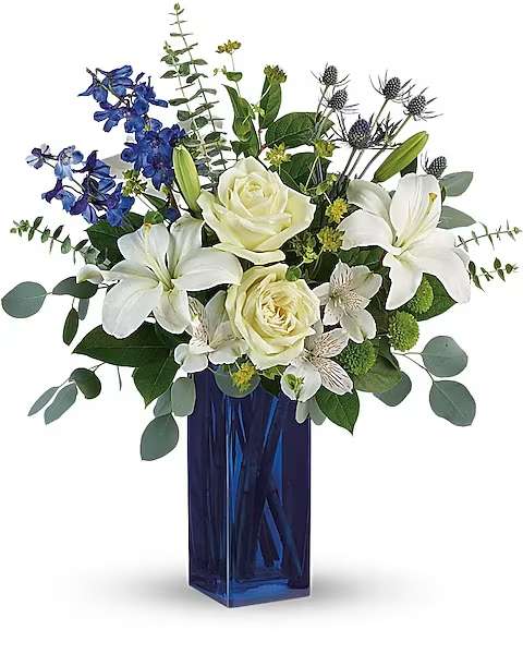 Teleflora's Calming Cobalt Bouquet - A classic for any occasion, this timeless bouquet of white roses and fragrant lilies in a rich, cobalt glass vase is sure to impress and delight.  This arrangement includes white roses, white asiatic lilies, white alstroemeria, green button spray chrysanthemums, blue eryngium, bupleurum, spiral eucalyptus, silver dollar eucalyptus, and lemon leaf. Delivered in a Blue Bunch vase.
