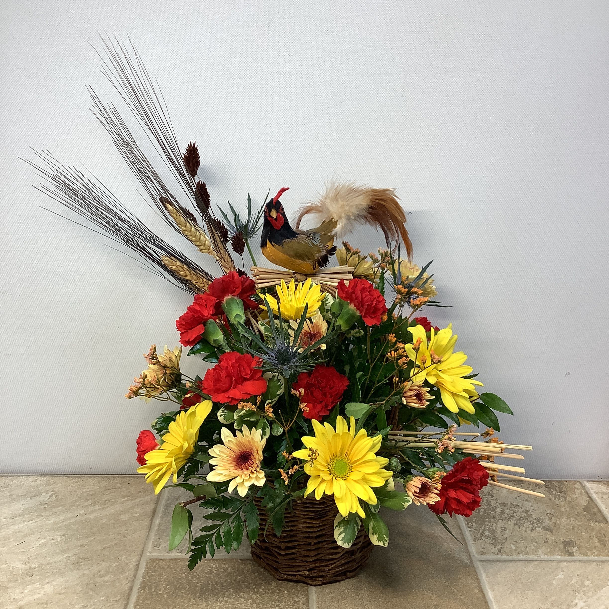 Sir Clucks-a-lot Sir Clucks-a-lot - A clever mix of daisies, mini carnations and thistle arranged in a wicker basket. Wheat grass and a feathered rooster add a touch of country charm. It measures 12” wide x 13” high.
