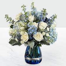 Ocean's Blue Bouquet * Vase will be changed* Ocean's Blue Bouquet * Vase will be changed* - This Bouquet is a gift that speaks from your heart to theirs. Reflecting the colors of the most majestic sky and the deep blue hues of running waters, this flower arrangement brings together white roses and white button poms with blue Bella Donna Delphinium and blue hydrangea, accented with Dusty Miller stems and lush greens. Presented in a keepsake modern deep blue glass vase with metallic banding