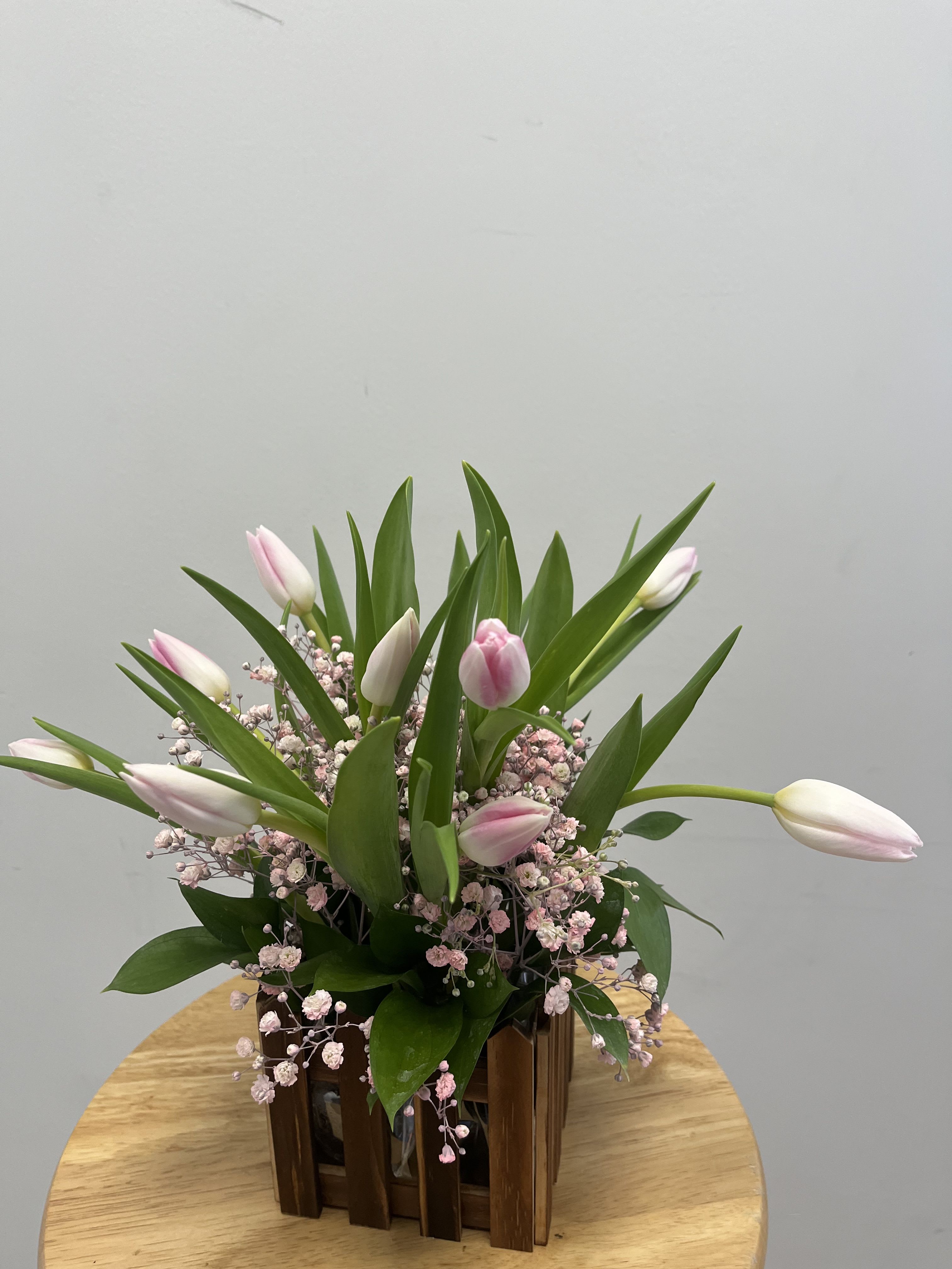 Mini Tulip Garden Mini Tulip Garden - This arrangement features pink tulips and pink baby breath with ruscus detailing in a wooden fence vase.