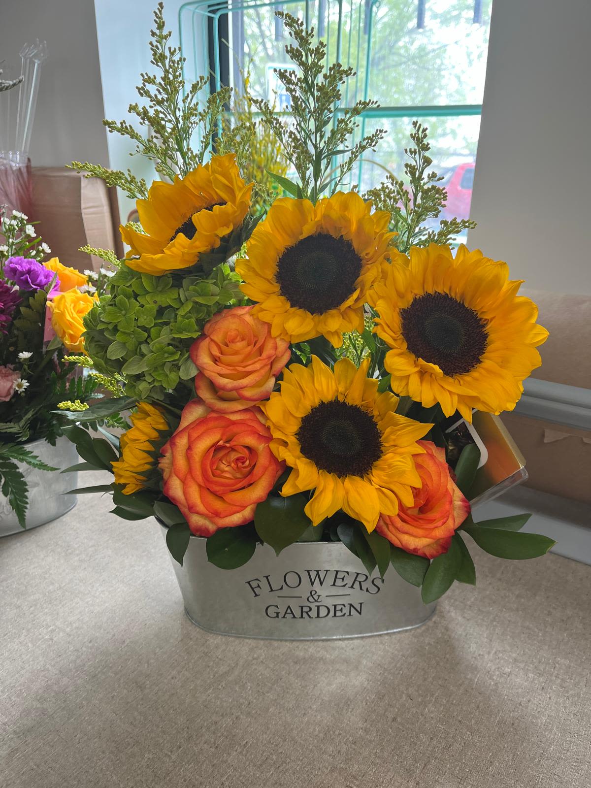 Happy Sunflower Happy Sunflower - Features sunflowers, magic roses, green hydrangeas, ruscus and goldenrods in a metal vase. Comes with one chocolate package.