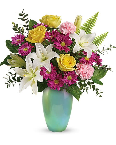 Teleflora's Aqua Artistry Bouquet - Spread sunshine and smiles with this bright yellow and bold purple bouquet, beautifully presented in a shimmering, iridescent aqua vase they'll enjoy for years to come!  Yellow roses, white asiatic lilies, light pink carnations, and purple daisy spray chrysanthemums are arranged with sword fern, parvifolia eucalyptus, and lemon leaf. Delivered in an Enamored with Aqua vase.