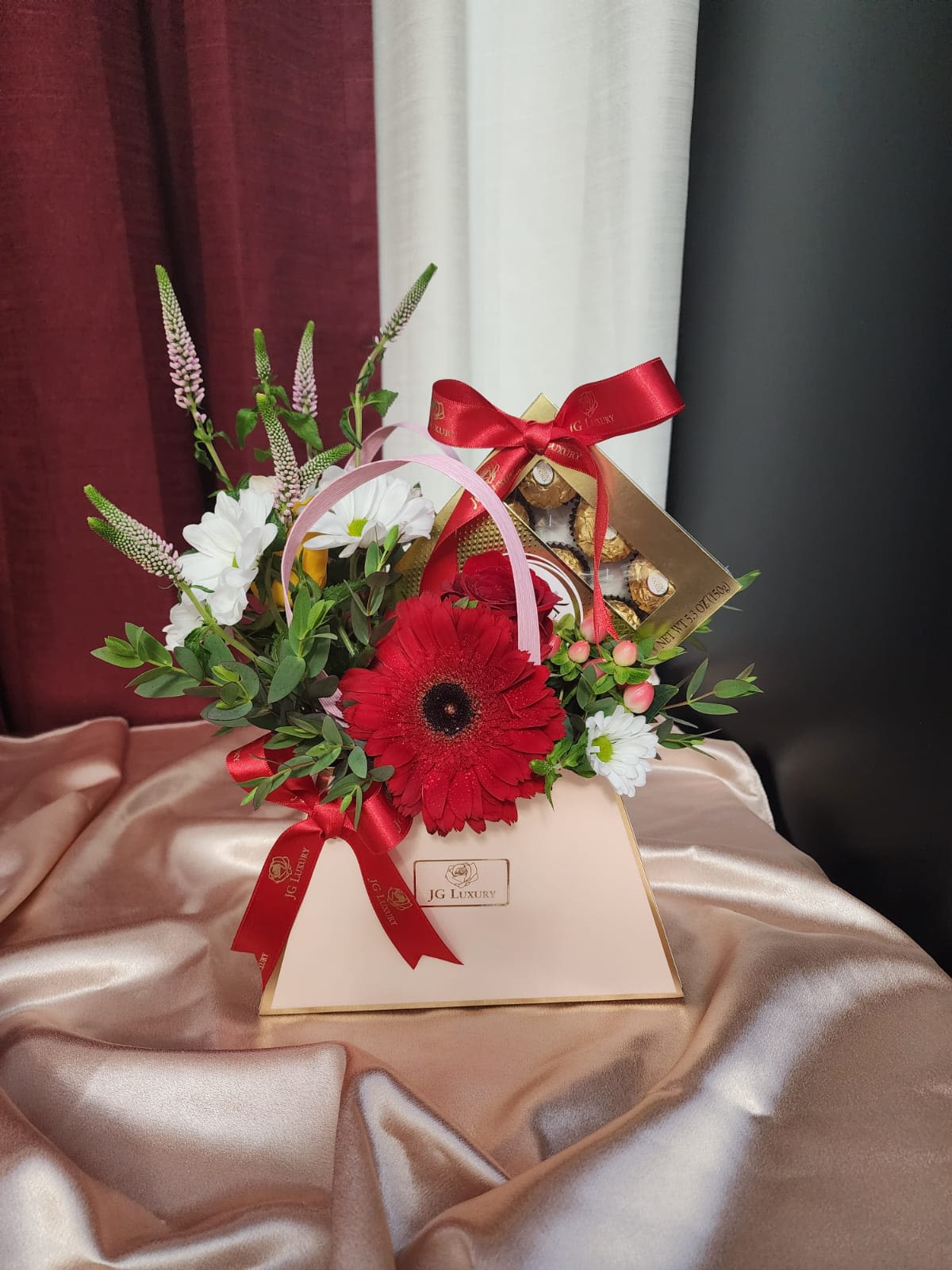 Designer’s Choice Handbag  - A stylish arrangement featuring a mix of the freshest blooms, elegantly presented in a designer handbag-style container. Each piece is uniquely crafted, so both the flower selection and container color may vary, ensuring a gift made with love and creativity. Includes a box of chocolates for a sweet finishing touch.