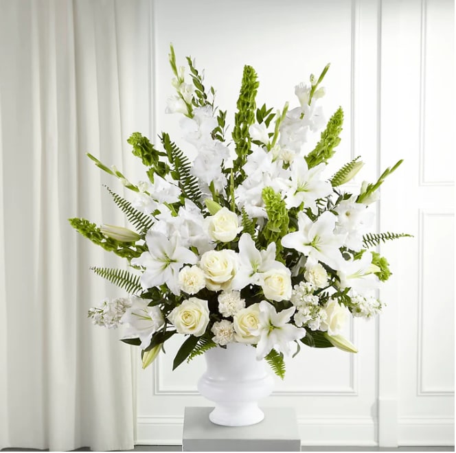 Morning Stars™ Arrangement - The Morning Stars Arrangment is a brilliant expression of peace and soft serenity. White roses, carnations, gladiolus, stock and Oriental lilies are accented with the bright green stems of Bells of Ireland and a gorgeous assortment of lush greens, while seated in a designer plastic urn to create a beautiful way to honor the life of the deceased. DETAILS 45&quot;h x 36&quot;w
