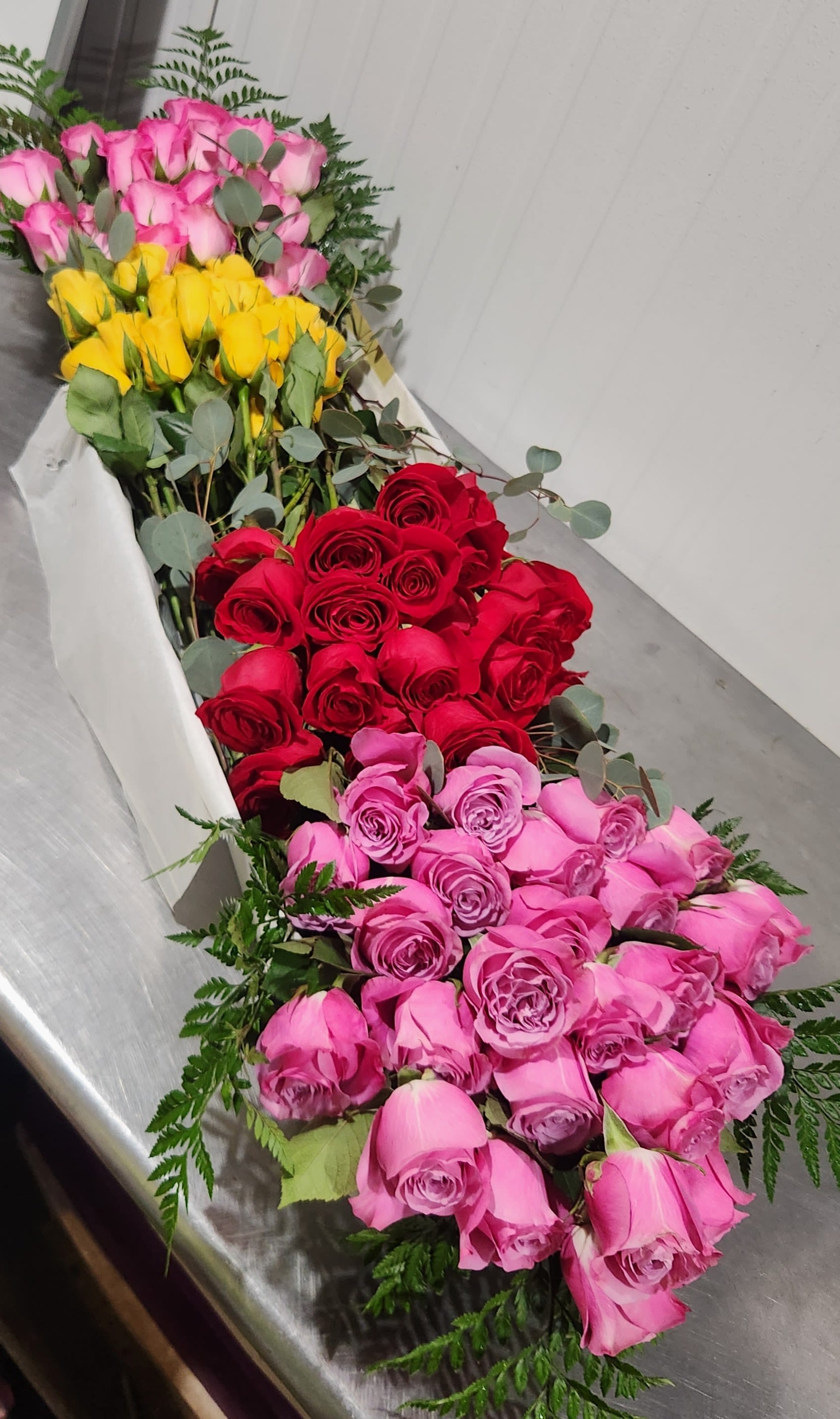 100 Rose Gift Box - A beautiful assortment of 100 roses adorned with greens and accented with a bow.