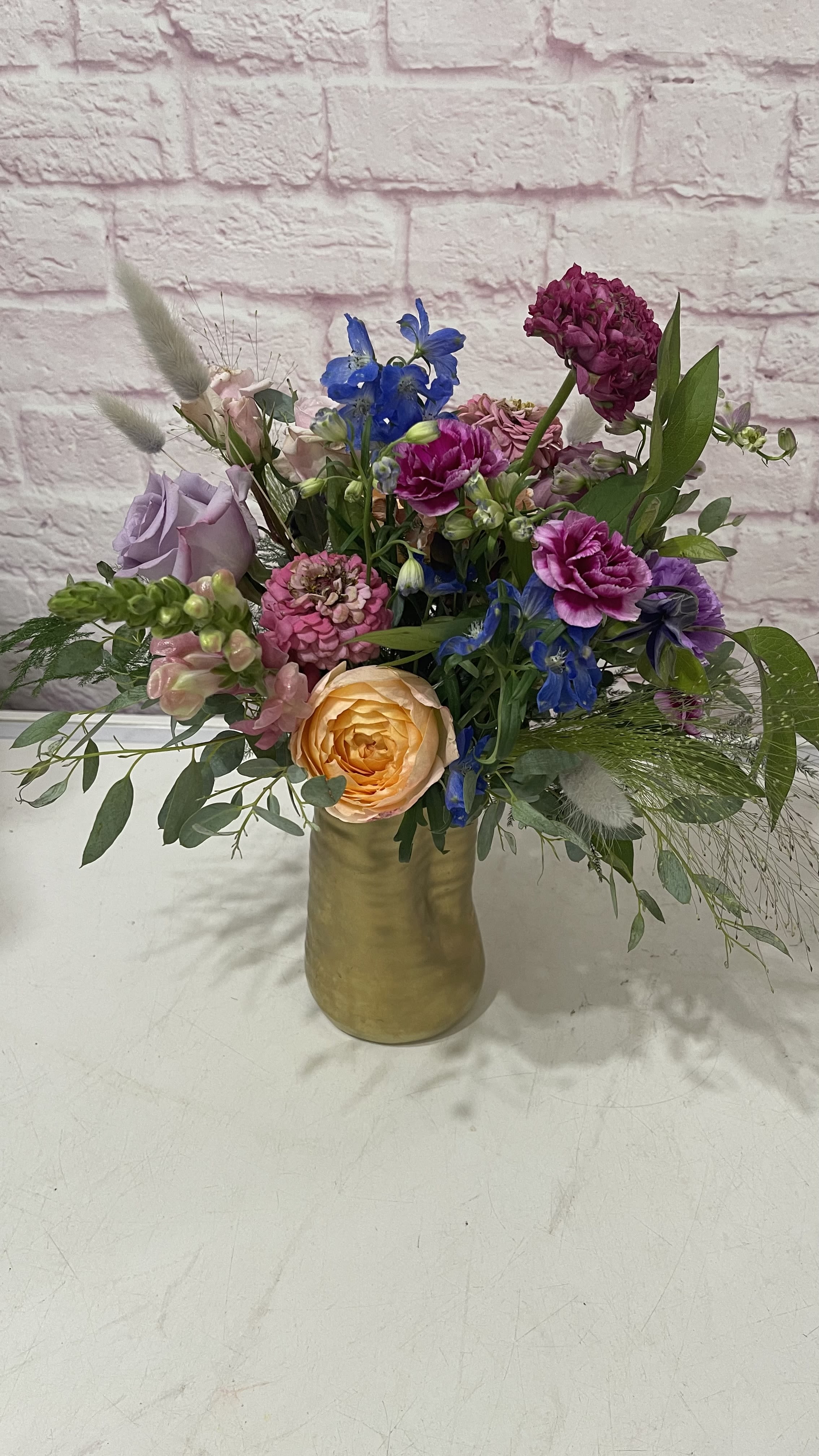Birds Of A Feather Birds Of A Feather - A mix is seasonal blooms in a gold clay distorted vase.