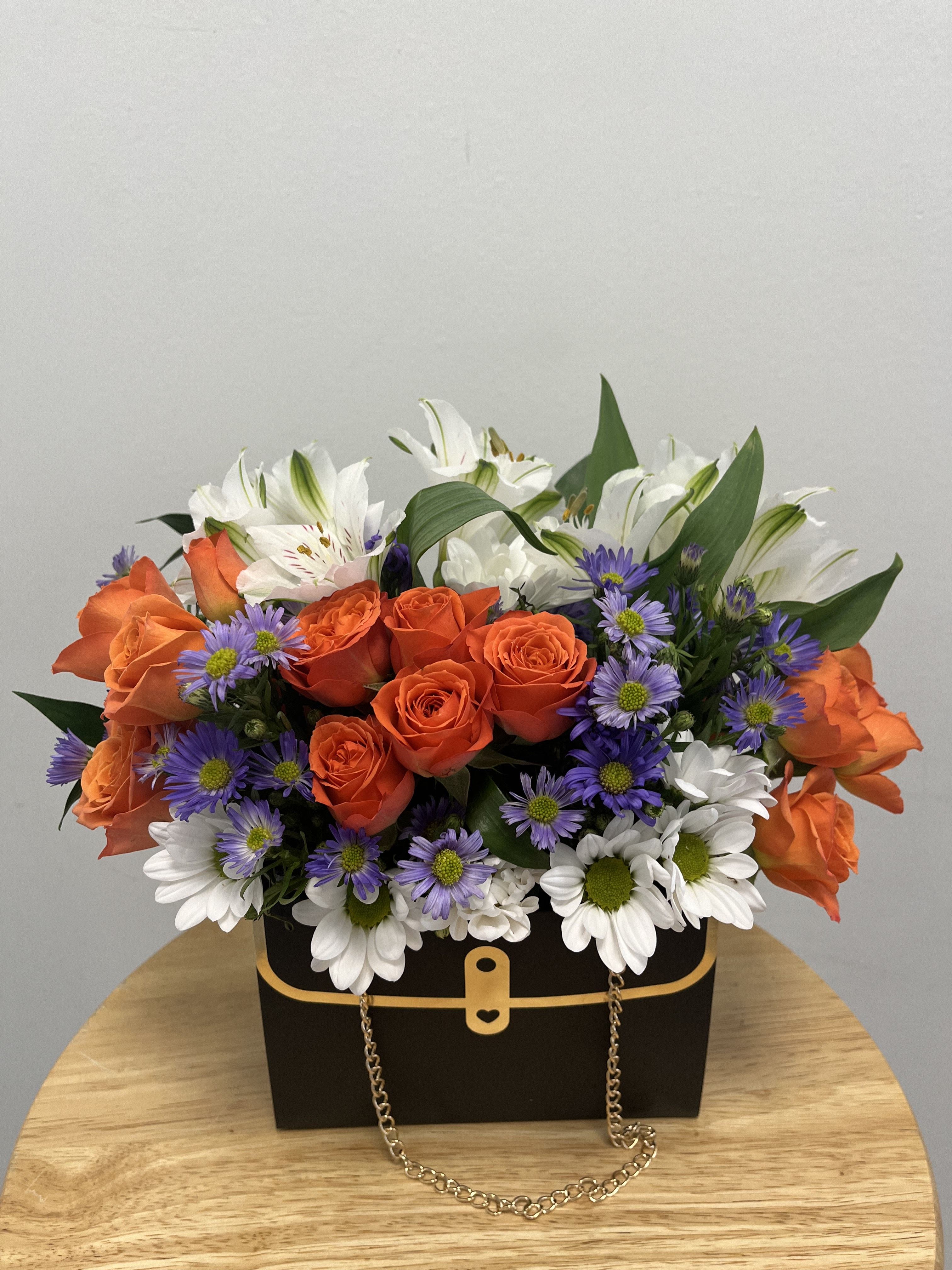 Orange Coquette Purse Orange Coquette Purse - This arrangement features orange spray roses, purple aster, white alstroemerias and white daises in a small black purse with gold detailing.