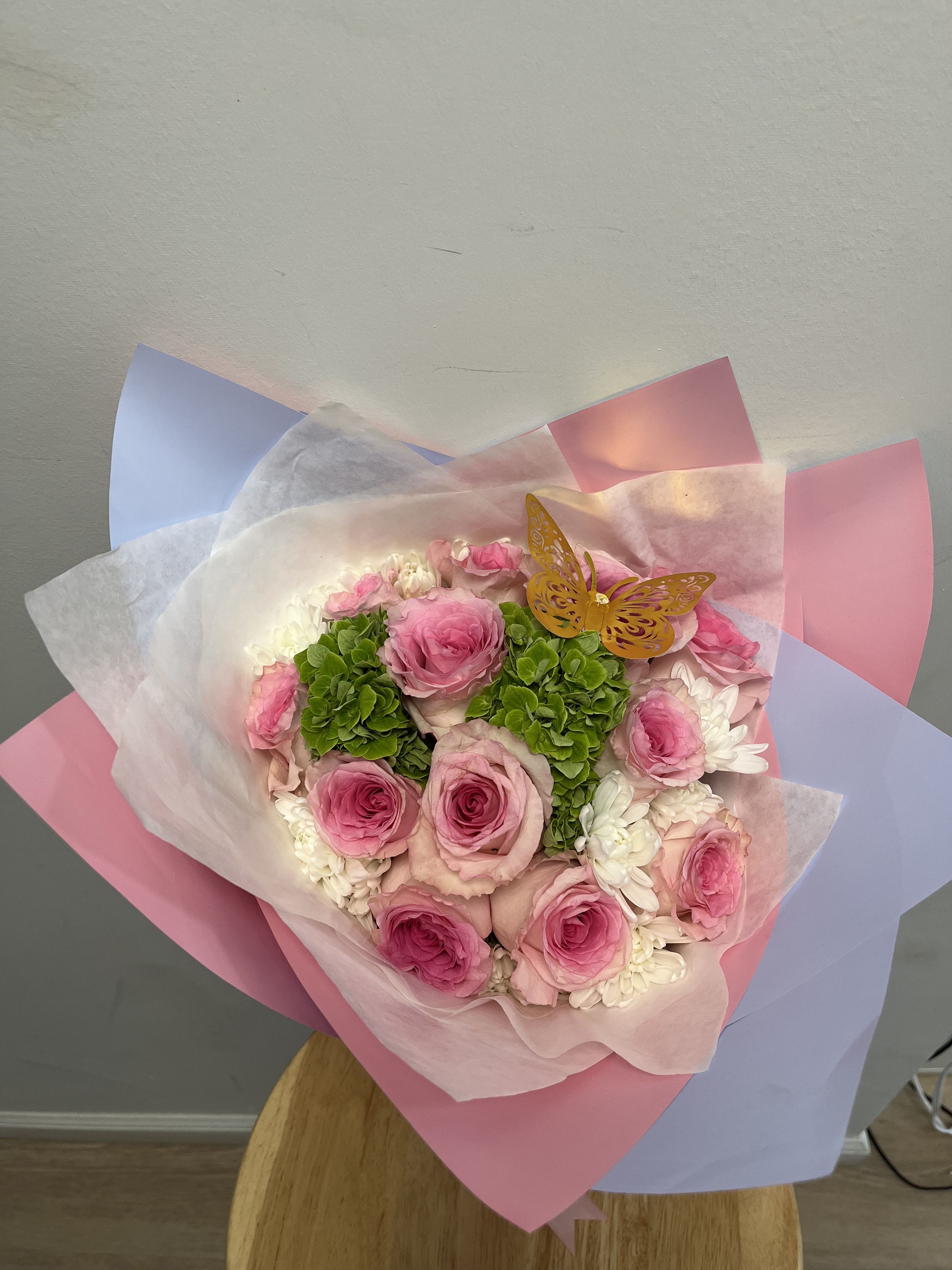 Garden Pink Bouquet Garden Pink Bouquet - This bouquet features pink rose, white chrysanthemums, green hydrangeas and is topped with a golden butterfly. Wrapped in pink, white and blue paper, this bouquet is perfect for any occasion.