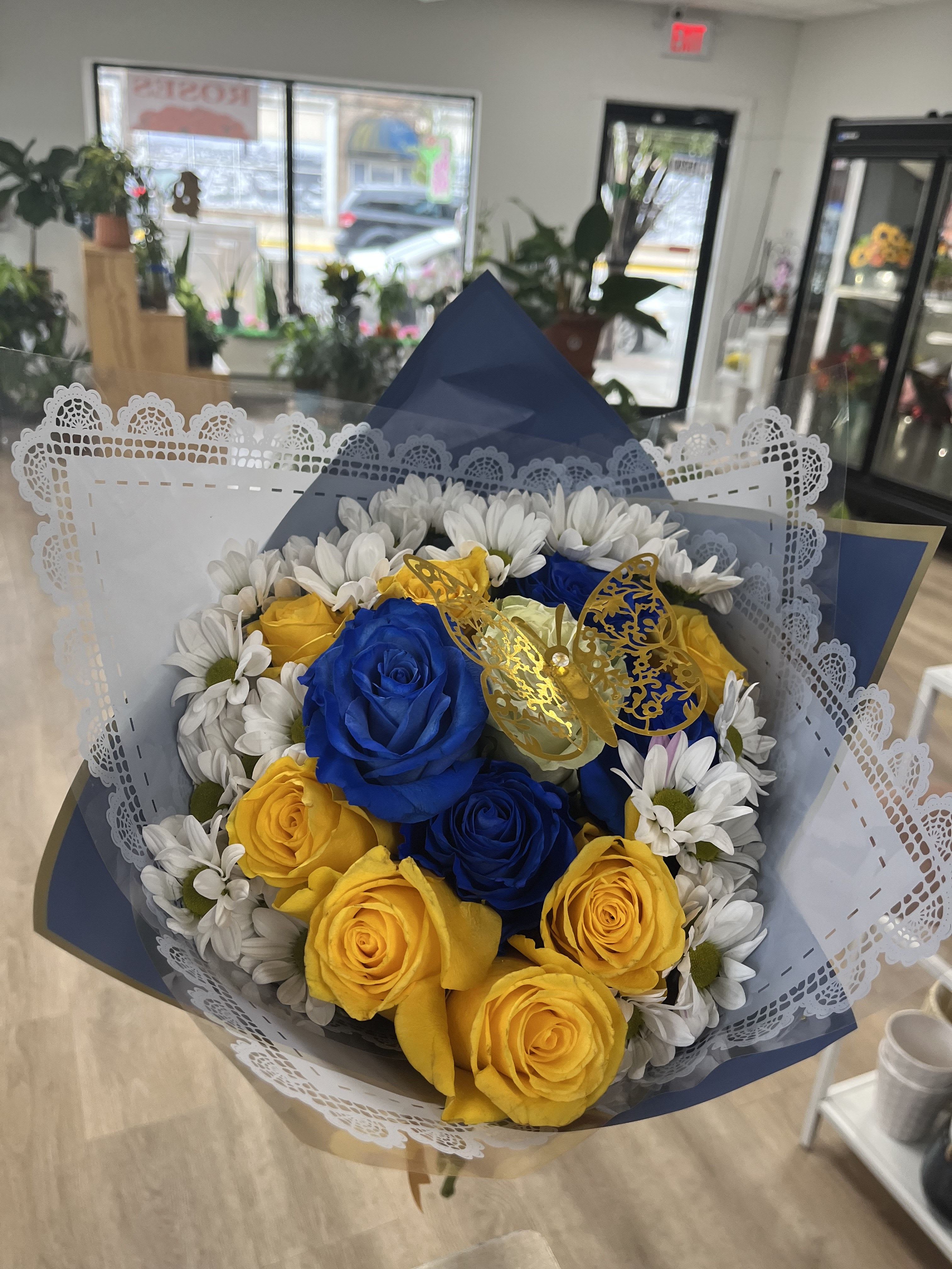 Graduation Bouquet Graduation Bouquet - This bouquet features blue roses, yellow roses, white daises, topped with a white rose and golden butterfly. Wrapped in blue and light blue lace paper, this bouquet is perfect for graduations and congratulations.