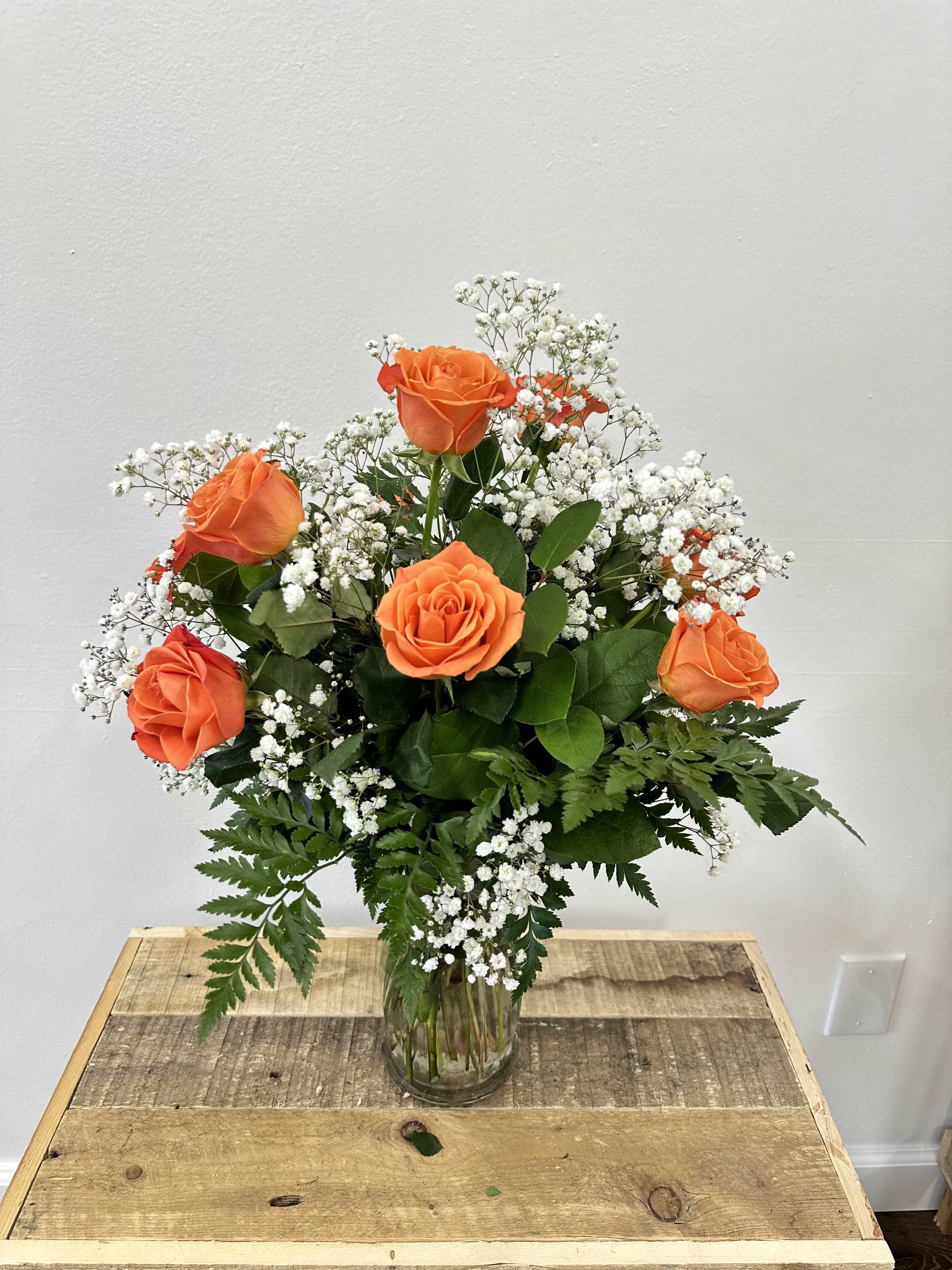 Orange Elegance - This stunning arrangment features a dozen premium red roses, complemented by delicate baby's breath and lush greenery, all elegantly displayed in a tall, clear glass vase. Perfect for romantic gestures, special occasions, or simply to add a touch of elegance to your home, this arrangement exudes sophistication and charm.