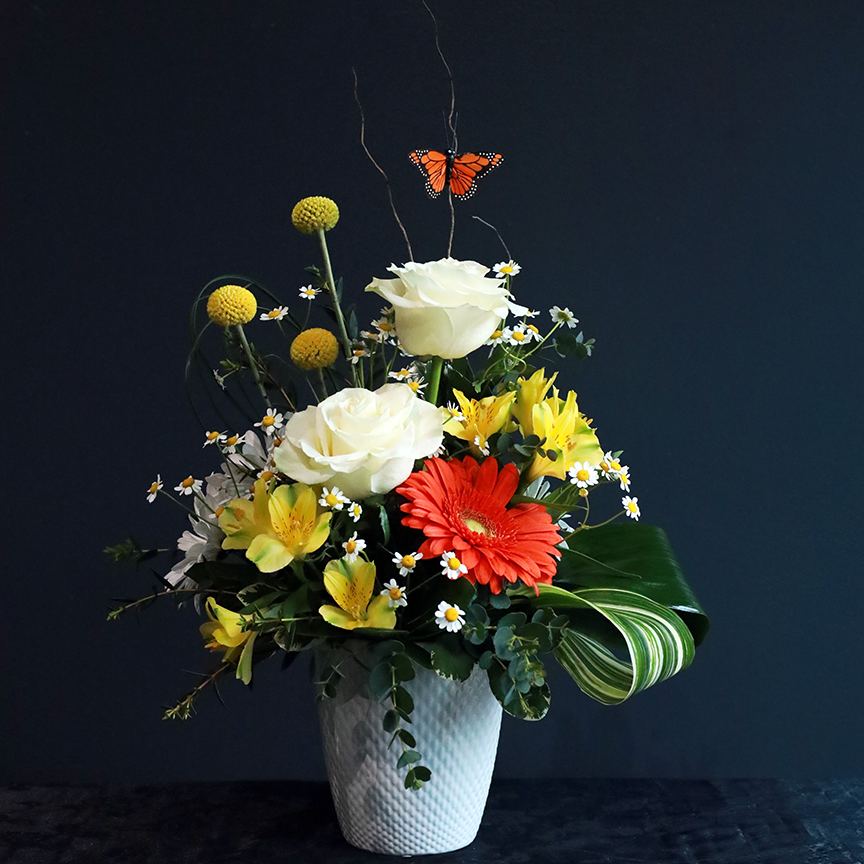 A Butterfly's Journey -  The &quot;A Butterfly's Journey&quot; arrangement is a thoughtful and uplifting choice to express your deepest condolences. This beautiful creation combines vibrant orange and white blooms, symbolizing warmth, peace, and the promise of new beginnings, while the butterfly symbolizes transformation and the continuation of life. The vibrant colors and the symbolic butterfly offer a gentle reminder that life continues to bloom, even in the face of loss.