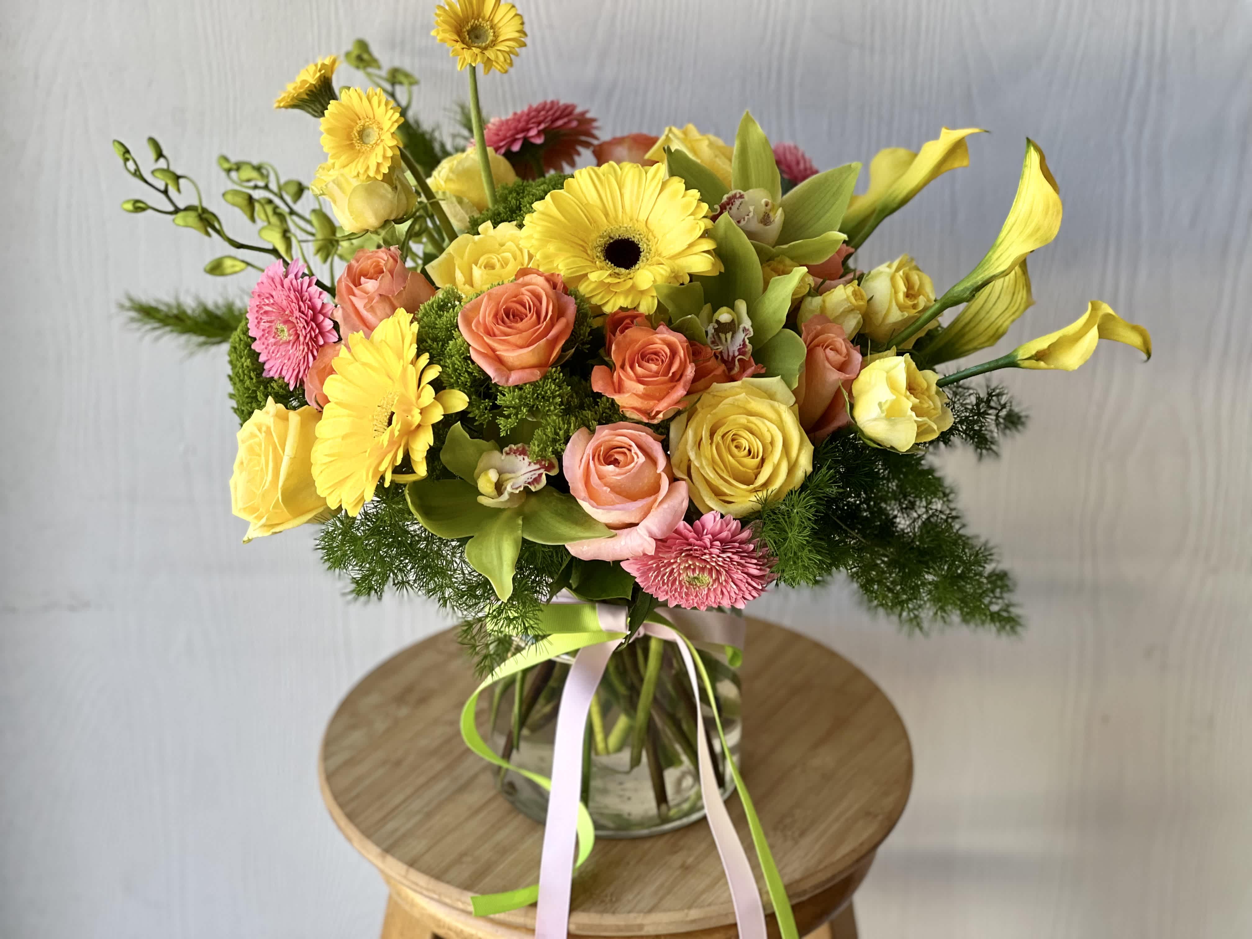 EC15 - Pretty and Bright - Bring some sunny cheer into your space with the vibrant and colorful flower arrangement &quot;Pretty and Bright.&quot; Featuring a delightful mix of sunny yellow, warm oranges, and fresh greens, and luxurious ming fern, makes a perfect pick-me-up for anyone who loves beauty and style. This luxurious gift is designed in a 8&quot; tall glass vase.