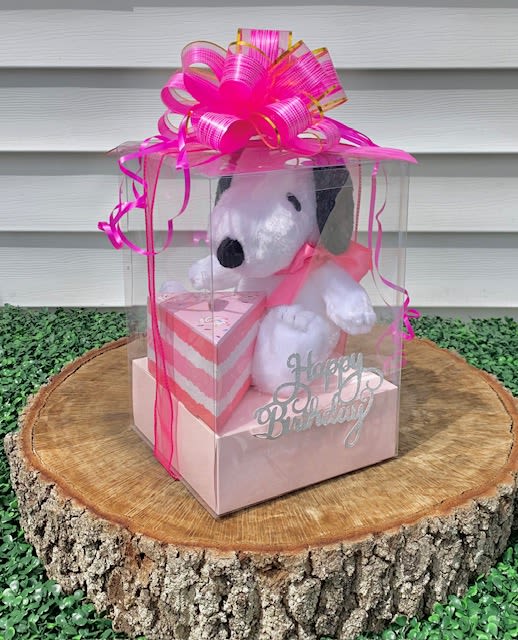 Snoopy Birthday Surprise  - A &quot;Happy Birthday&quot; clear gift box with a dog plushie and a cake-slice-shaped box filled with chocolates is the perfect mix of adorable and indulgent!  A sleek, transparent box elegantly wrapped with festive ribbon, showcasing its delightful contents inside. The plush dog—soft, cuddly, and irresistibly charming—sits front and center, offering warmth and joy. Next to it, the cake-slice-shaped box adds a whimsical touch, designed like a perfect slice of cake, complete with decorative details that mimic frosting and layers. Inside, decadent chocolates await—perhaps truffles, caramel-filled treats, or gourmet selections—making every bite feel like a birthday celebration.  It’s both visually appealing and heartwarming, making it a wonderful way to bring joy to someone’s special day. Would you like suggestions on how to enhance the presentation or customize it?