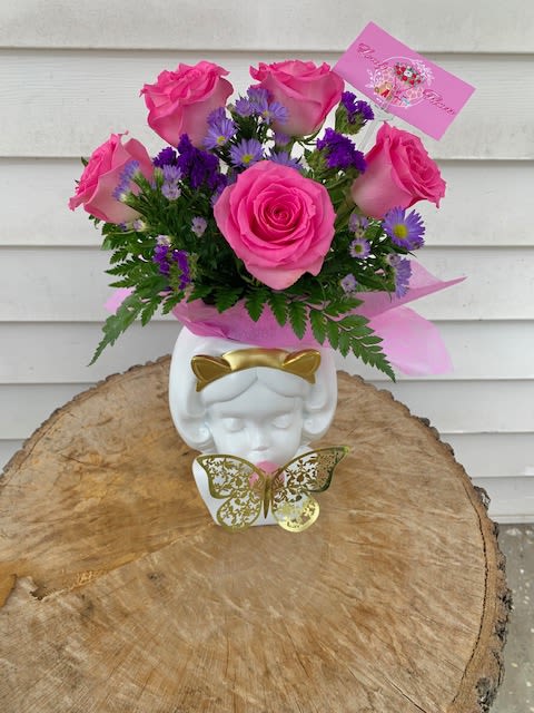 Bubble Gum Girl - Whimsical and unexpected, this vase makes an instant statement. Picture a sculpted porcelain head of a young girl, eyes closed in playful concentration, cheeks puffed gently as she blows a glossy pink bubble that protrudes just beyond her lips. The smooth ceramic surface is finished in a soft matte blush or ivory, giving it a dreamy, almost storybook quality.  The top of the vase—where her hair would be—is cleverly hollowed out and overflowing with roses: tightly spiraled blooms in pastel shades of pink, cream, and soft coral. The effect is both surreal and sweet, as if her thoughts have bloomed into roses or her imagination is quite literally flowering.  It’s the kind of piece that would charm in a modern nursery, add a touch of mischief to a flower shop window, or make a cheerful gift for someone with a quirky sense of style.