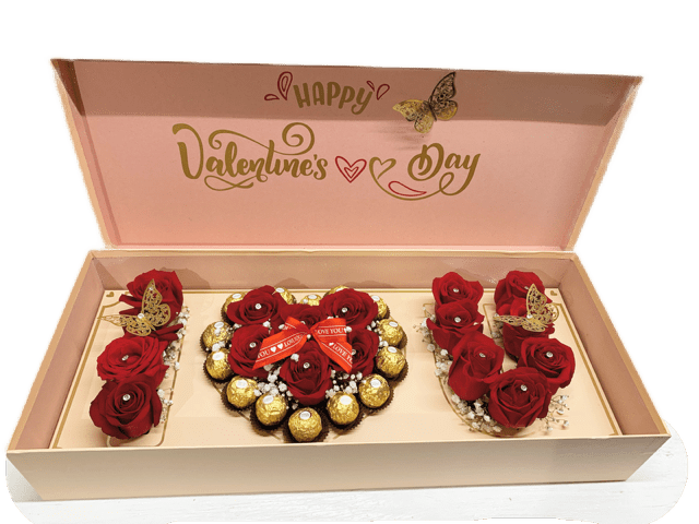Valentines Box - This Valentine’s Day arrangement is the definition of sweet romance wrapped in elegance. Picture a beautifully crafted keepsake box, perhaps velvet-lined or with a soft matte blush finish, its lid slightly ajar to reveal a stunning duo of delights inside.  On one side, a bed of fresh red roses, their velvety petals in full bloom, arranged with care so their heads peek just above the rim—lush, fragrant, and completely captivating. Nestled delicately between some of the blooms are tiny accents like baby's breath or miniature heart picks, adding subtle sparkle and charm.  On the other side, an array of gourmet chocolates rests in gold-foiled paper cups—rich truffles dusted in cocoa, silky caramels enrobed in dark chocolate, maybe even heart-shaped pralines with raspberry filling. It’s indulgence and affection, side by side.  The box is tied together with delicious chocolates, butterflies and diamond pins.   