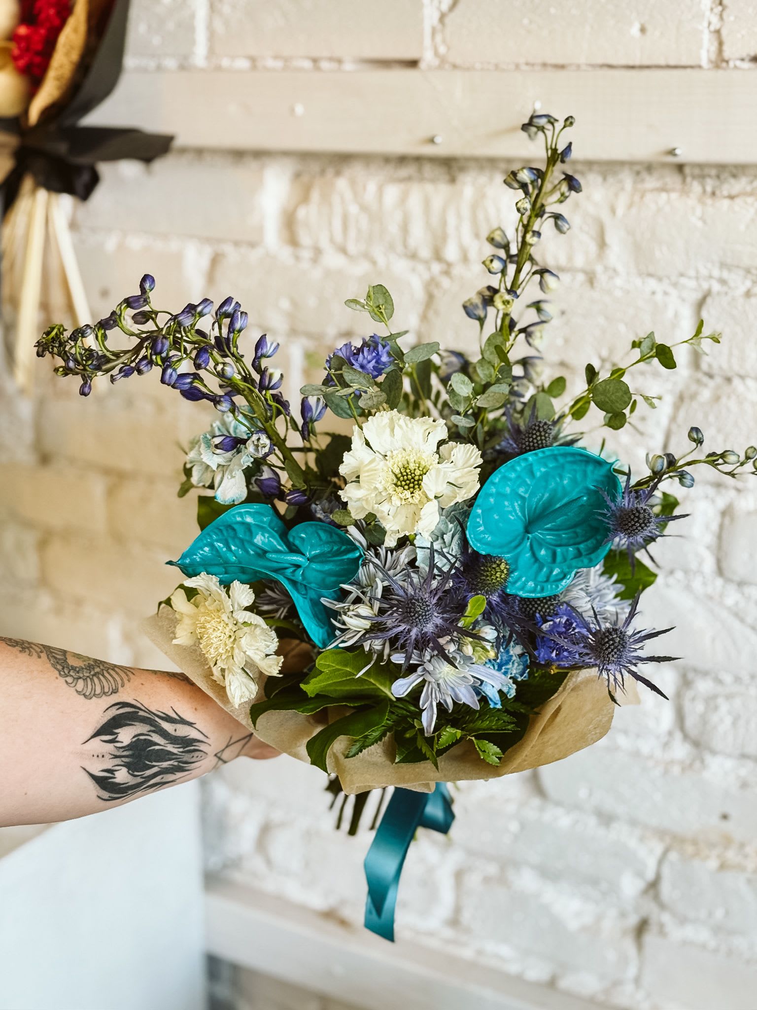 Boyfriend Material - Celebrate love in all its vibrant hues with Boyfriend Material, a stunning arrangement inspired by the gay/MLM pride flag. Featuring rich shades of green, blue, and turquoise, this bouquet blends lush, textured blooms and greenery to create a bold and beautiful statement for Pride Month. Perfect for gifting to a partner, honoring friendship, or treating yourself, Boyfriend Material is a colorful reminder that love between men is powerful and worthy of celebration. This product is a hand-tied bouquet. Want it in a vase? Add one to make it extra special!