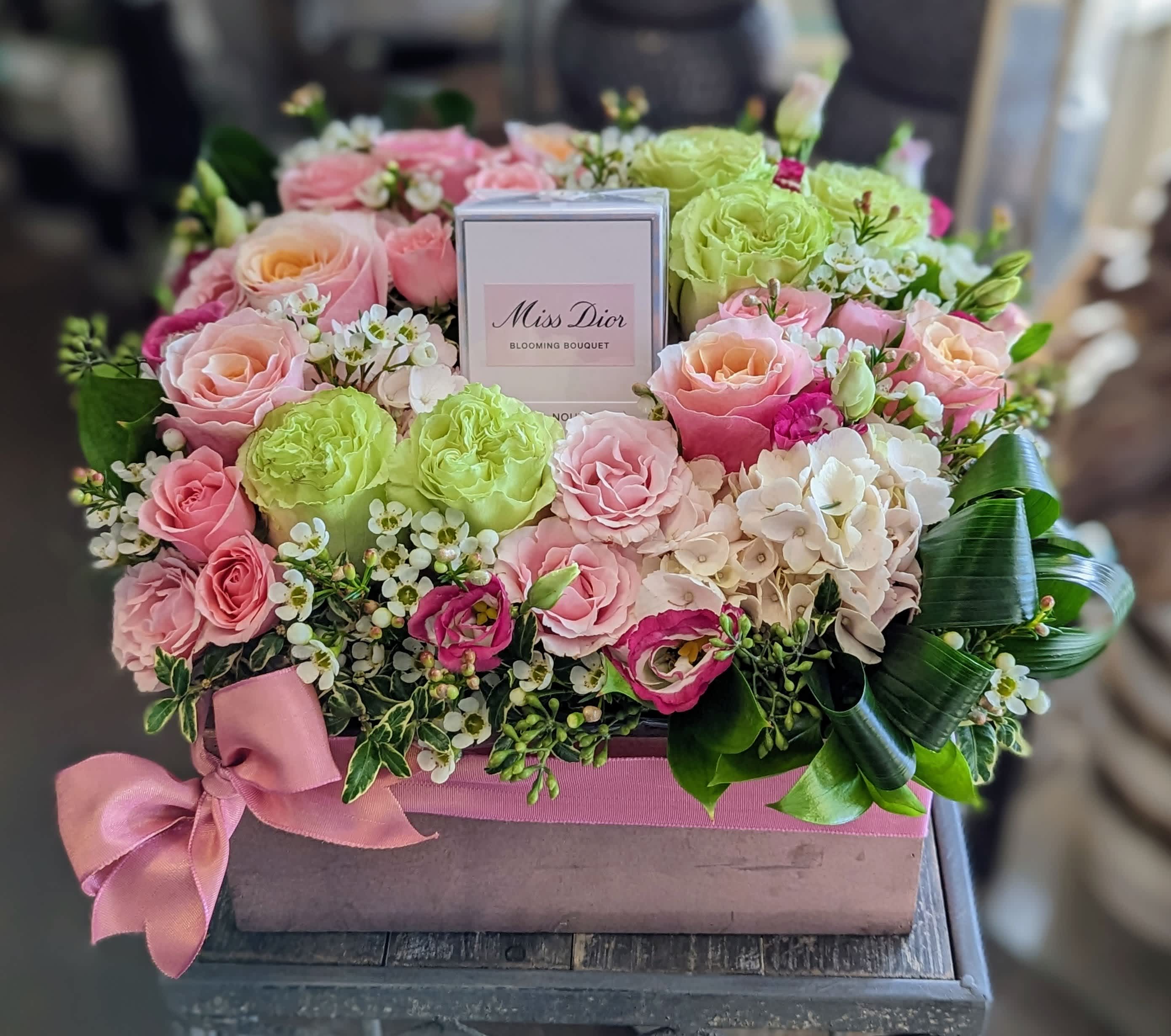 Coco- Perfume Not Included Coco- Perfume Not Included - Coco by Windmill Floral Expressions in Las Vegas is a love letter in bloom—where haute couture meets horticultural artistry. This luxurious boxed floral arrangement is designed to surround their favorite fragrance with timeless elegance, making every moment feel like a scene from Paris. A lush medley of pale pink garden roses, vibrant green roses, soft peach blooms, and delicate waxflower is artfully arranged to cradle a bottle of perfume at its heart (fragrance not included). Each bloom is thoughtfully chosen to evoke romance, style, and the essence of modern femininity. Presented in a rose gold wood box, finished with a soft satin ribbon, Coco is the perfect gift for birthdays, anniversaries, Mother’s Day, or any occasion where you want to give something truly unforgettable. Handcrafted in Las Vegas and available for same-day flower delivery across Las Vegas and Henderson. The fragrance if not included. You provide the perfume and we will customize the arrangement to your color palette.