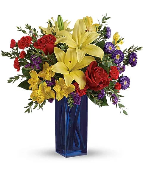 Teleflora's Flying Colors Bouquet - Celebrate any occasion with flying colors! This bold, beautiful bouquet of red roses, yellow lilies and purple asters in a rich cobalt glass vase will make their hearts soar.  This colorful arrangement includes red roses, yellow asiatic lilies, yellow alstroemeria, red miniature carnations, purple matsumoto asters, purple sinuata statice, parvifolia eucalyptus, and lemon leaf. Delivered in a Blue Bunch vase.