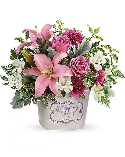 Teleflora's Monarch Garden Bouquet - Sure to make mom's heart flutter, this sweet ceramic planter features a charming butterfly motif, a rustic rope handle, and a gorgeous bouquet of lavender roses and pink lilies.  This arrangement features lavender roses, pink asiatic lilies, white alstroemeria, purple cushion spray chrysanthemums, dusty miller, leatherleaf fern, and pitta negra. Delivered in a Monarch Garden planter.