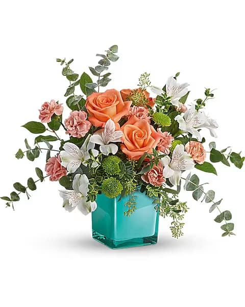 Teleflora's Sunset Splash Bouquet - Inspired by the warm peach skies and crystal blue waters of a tropical sunset, this fun-filled rose bouquet adds a splash of happiness to any occasion!  This delightful arrangement features peach roses, white alstroemeria, peach miniature carnations, green button spray chrysanthemums, spiral eucalyptus, seeded eucalyptus, oregonia, and lemon leaf. Delivered in an Aqua Color Splash Cube.